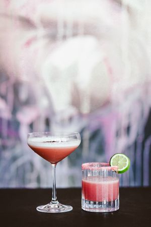 Pink cocktails garnished with lime slices on a bar counter.