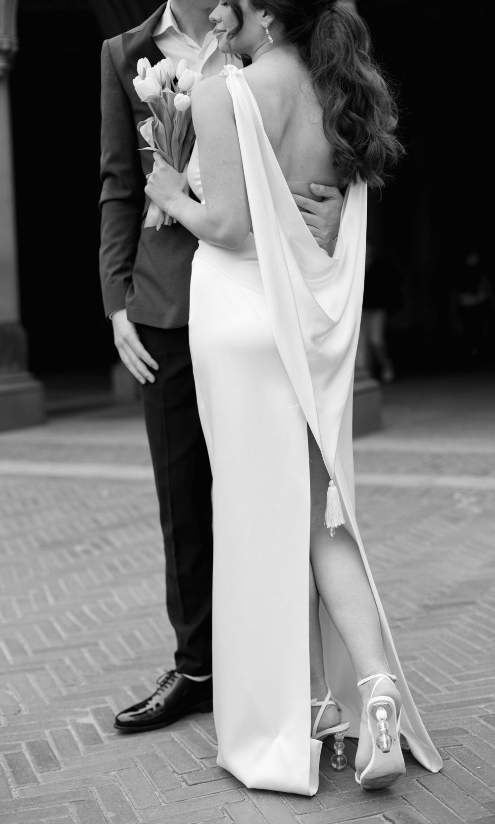 Elegant wedding couple holding white flowers with bride wearing flowing white dress with cape detail.
