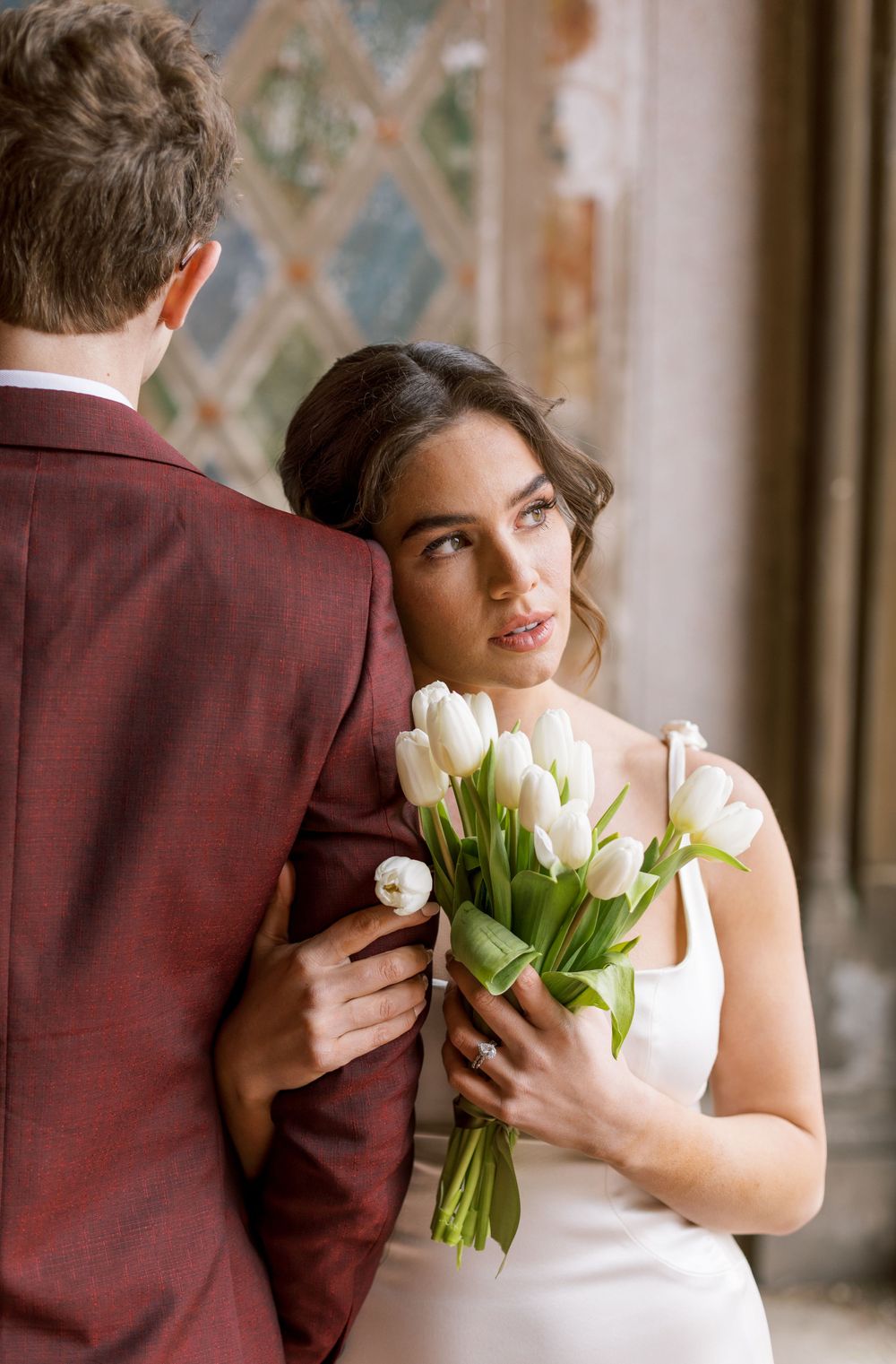 Intimate wedding portrait with white tulip bouquet against decorative architectural backdrop.