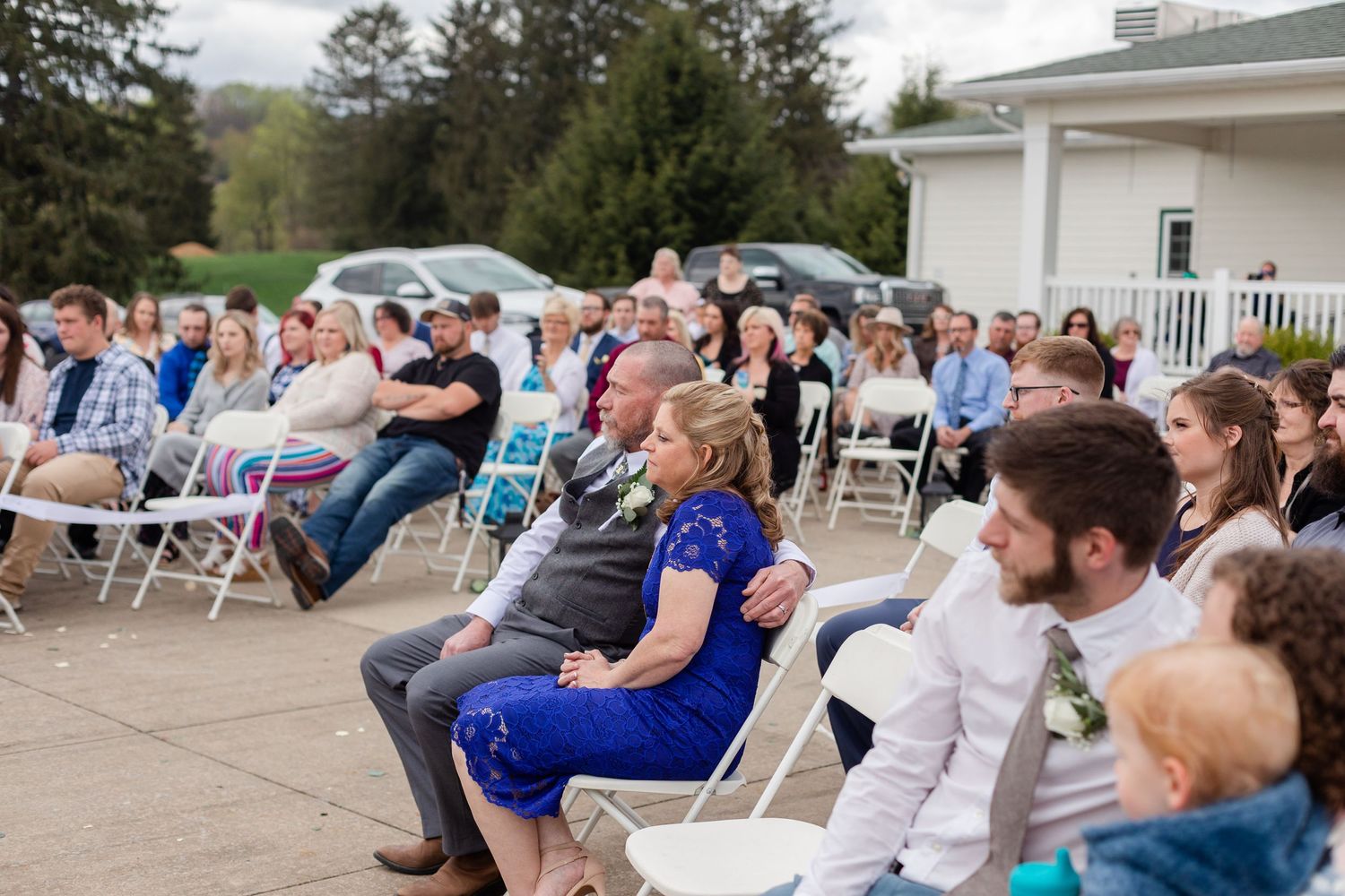 Wedding guests seated outdoors watching a ceremony under cloudy skies.