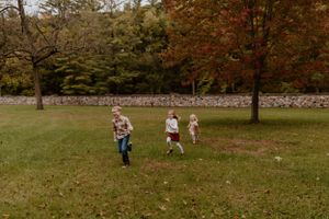 Children playing and running on grass in an autumn park with stone wall.