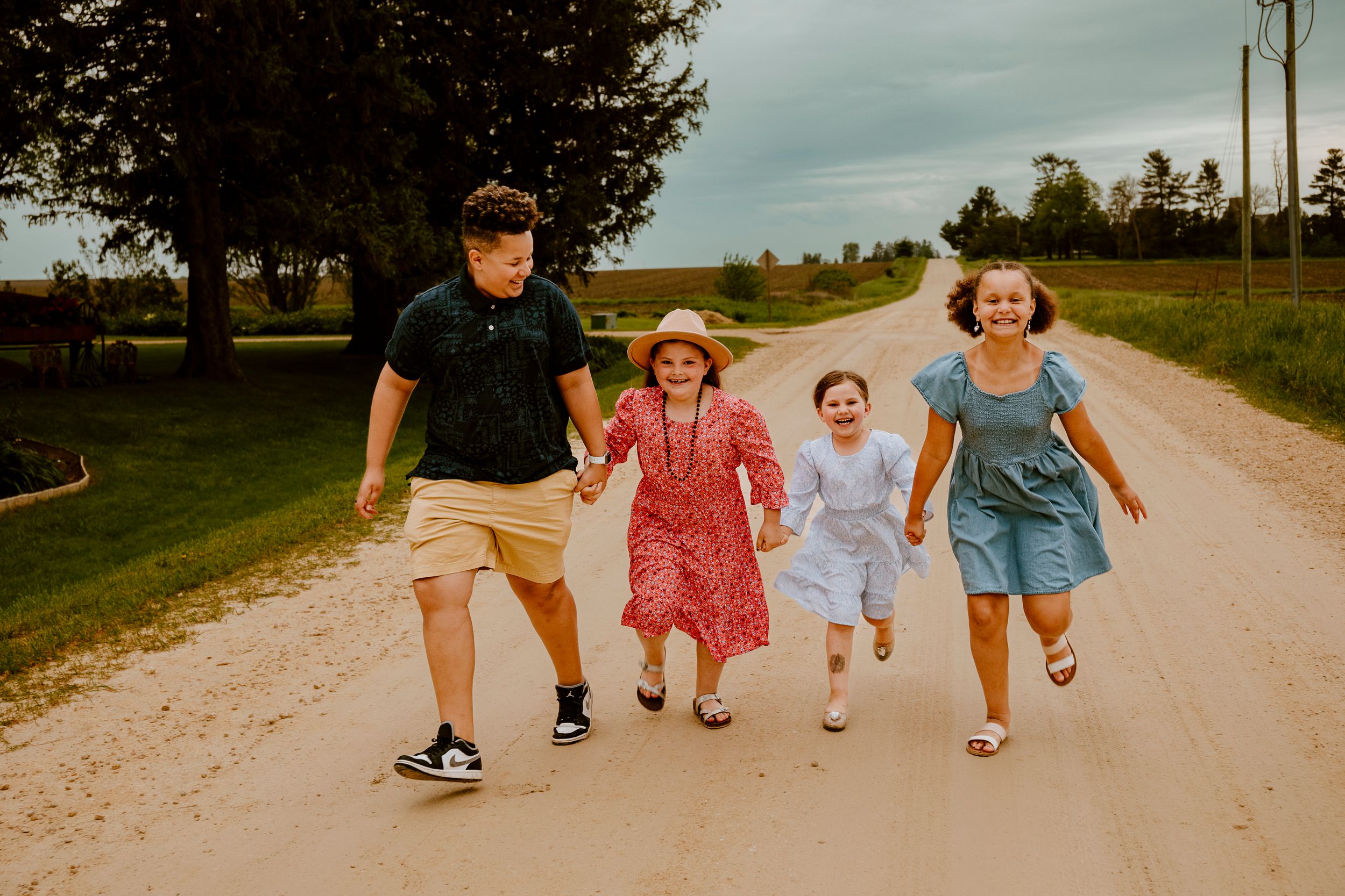 A group runs and laughs together down a rural dirt road on a summer day, creating a joyful candid moment.