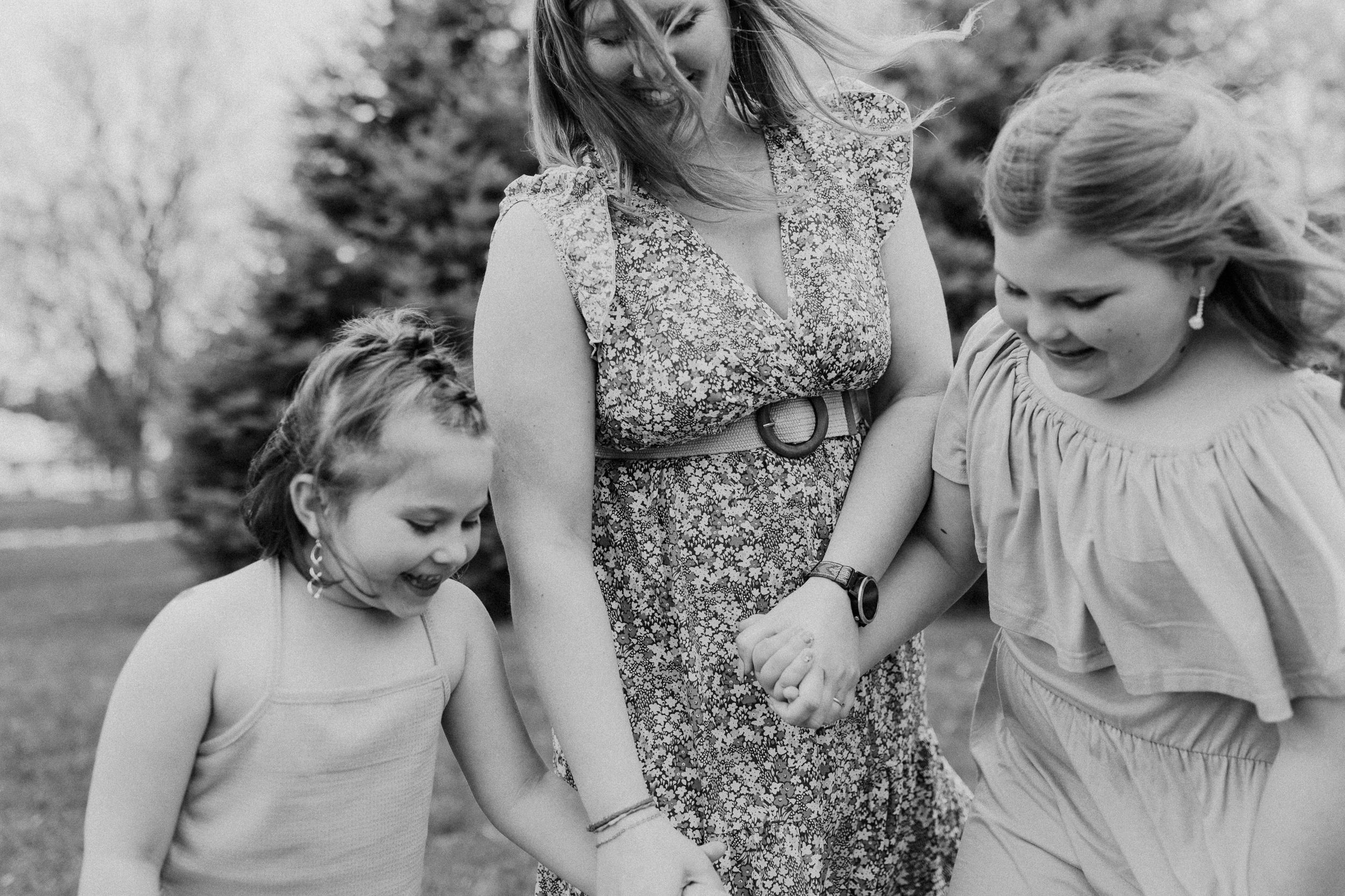 Three people in flowing dresses share a joyful moment together in a grassy outdoor setting.