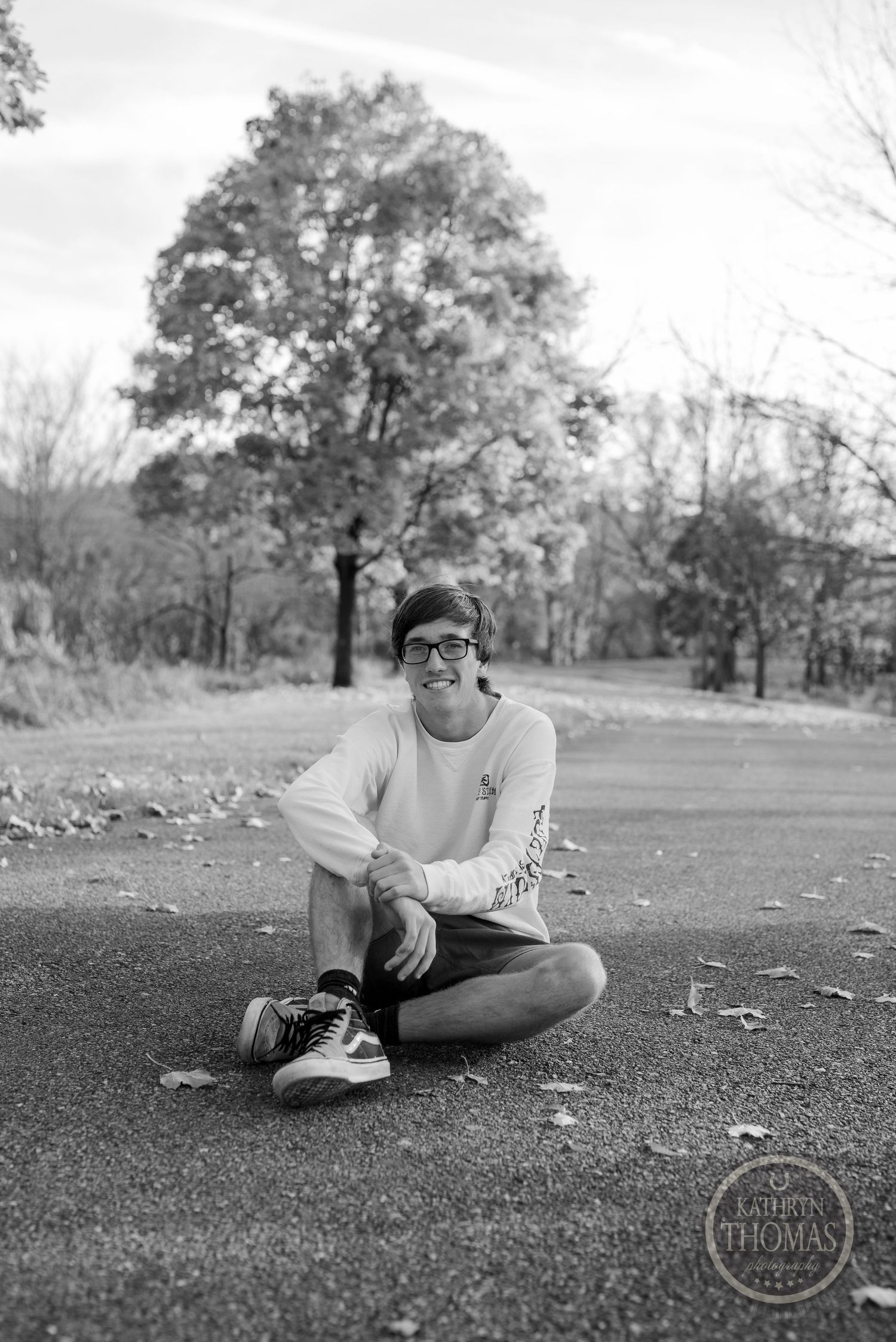 Black and white portrait of person sitting on path wearing casual attire.