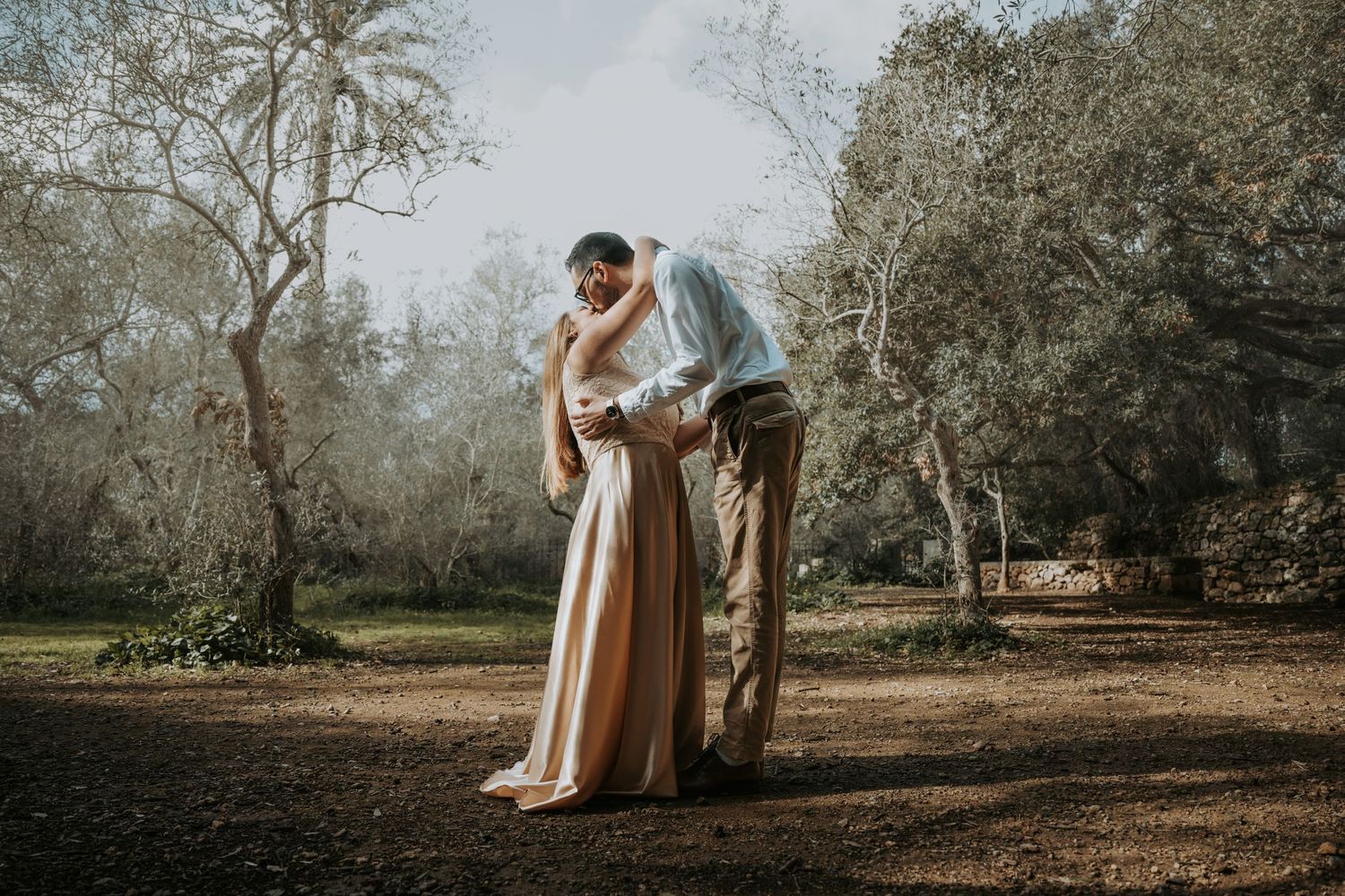 Romantic outdoor maternity photo session in a natural setting with soft lighting and trees.