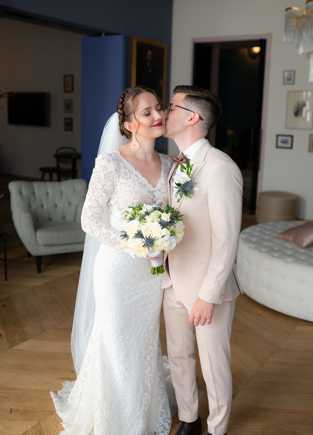 Bride and groom share a tender kiss indoors, bride holding white and blue bouquet.