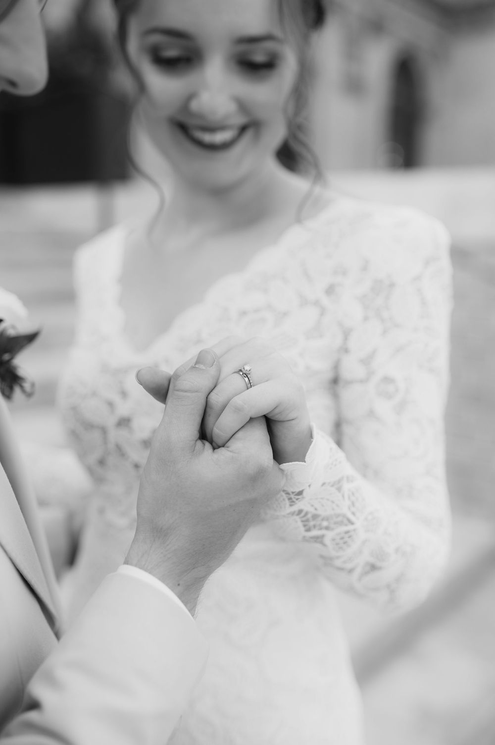 Black and white close-up of bride and groom holding hands, showing diamond engagement ring.
