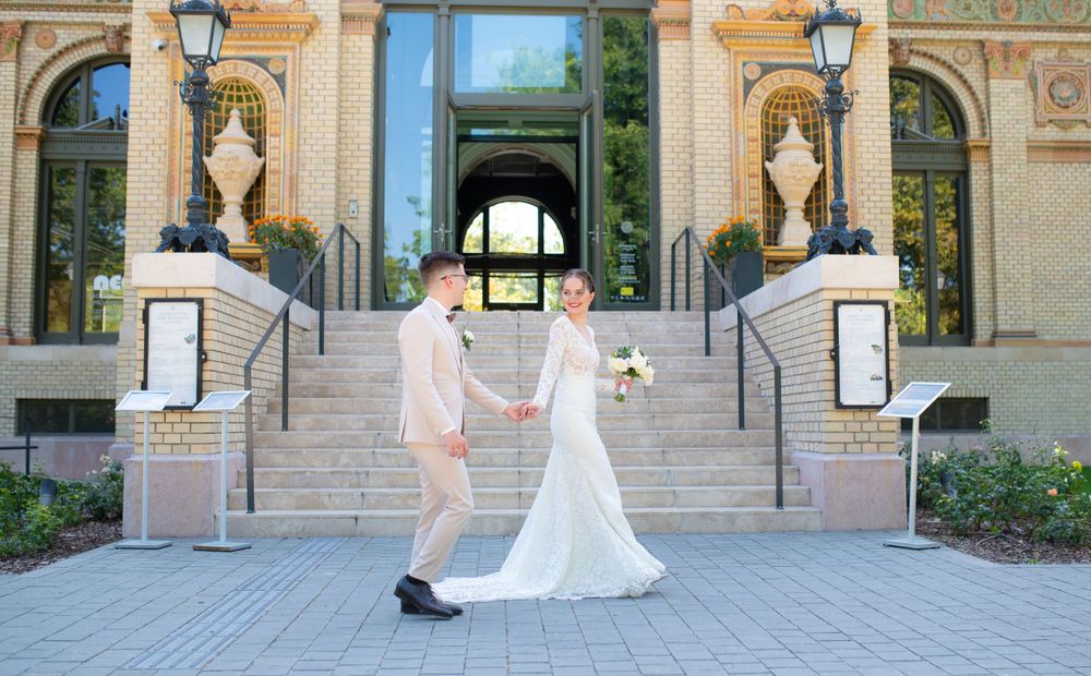 Elegant bride and groom holding hands on steps of a classic brick building on their wedding day.
