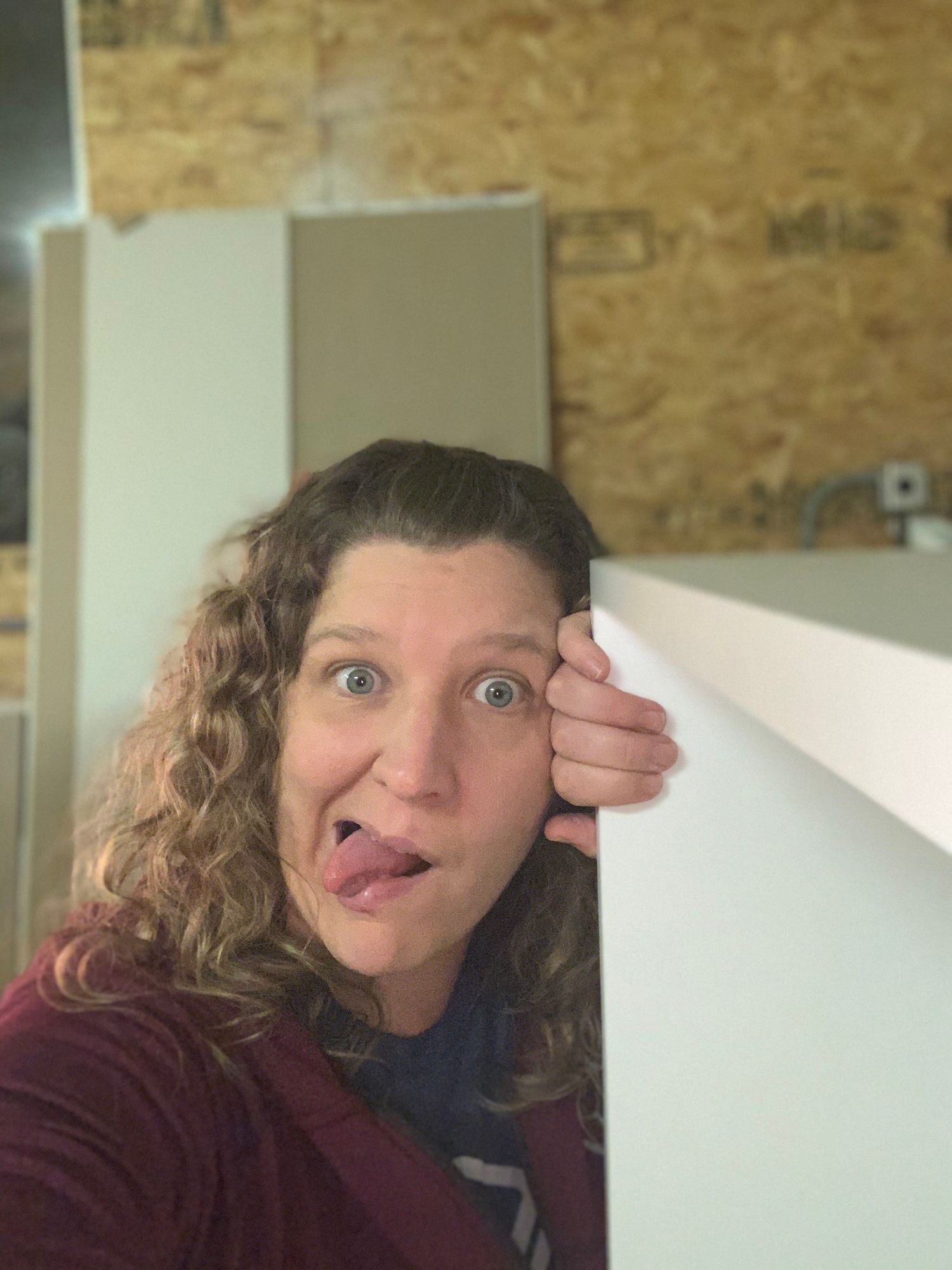 Playful selfie taken peeking around a white wall in an interior space.