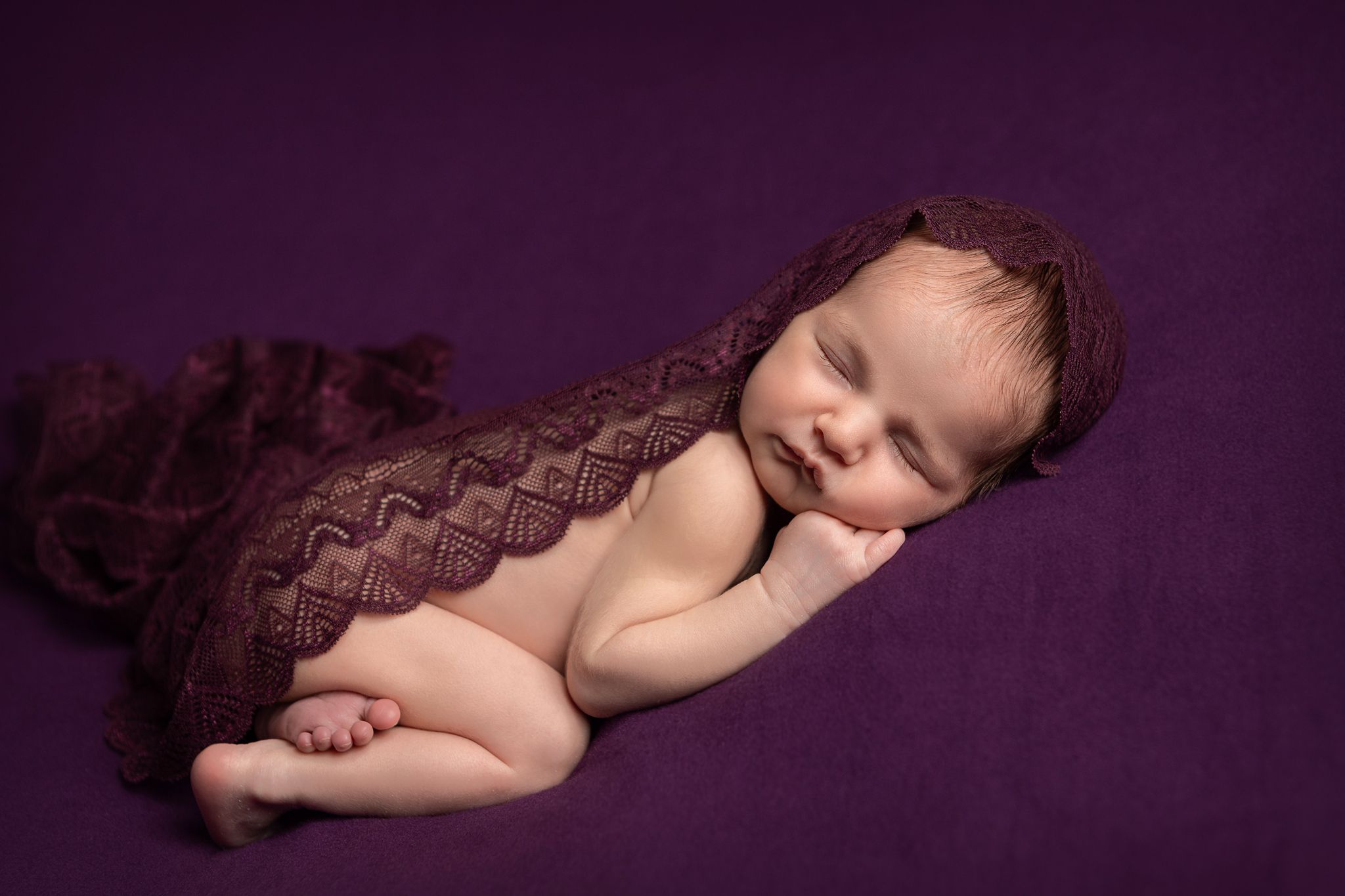 Newborn girl, sleeping on a purple blanket with purple lace