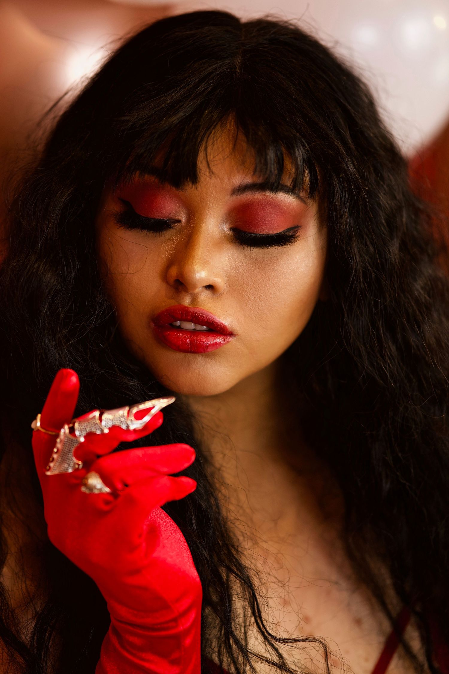 Edgy boudoir portrait of a woman with dramatic red eye makeup, red lips, and gloves creating a bold romantic look.
