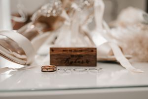 Wedding rings and ornate sepia-toned details with a wooden name plate create a romantic vintage bridal still life.