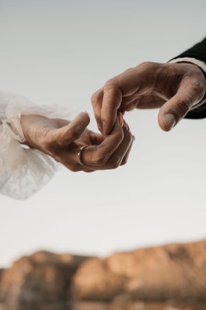 Two hands gently touch while exchanging a ring against a backdrop of desert mountains during a romantic moment.