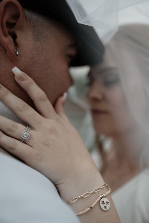 Close-up of a tender wedding moment showing delicate jewelry and an engagement ring under a white veil.