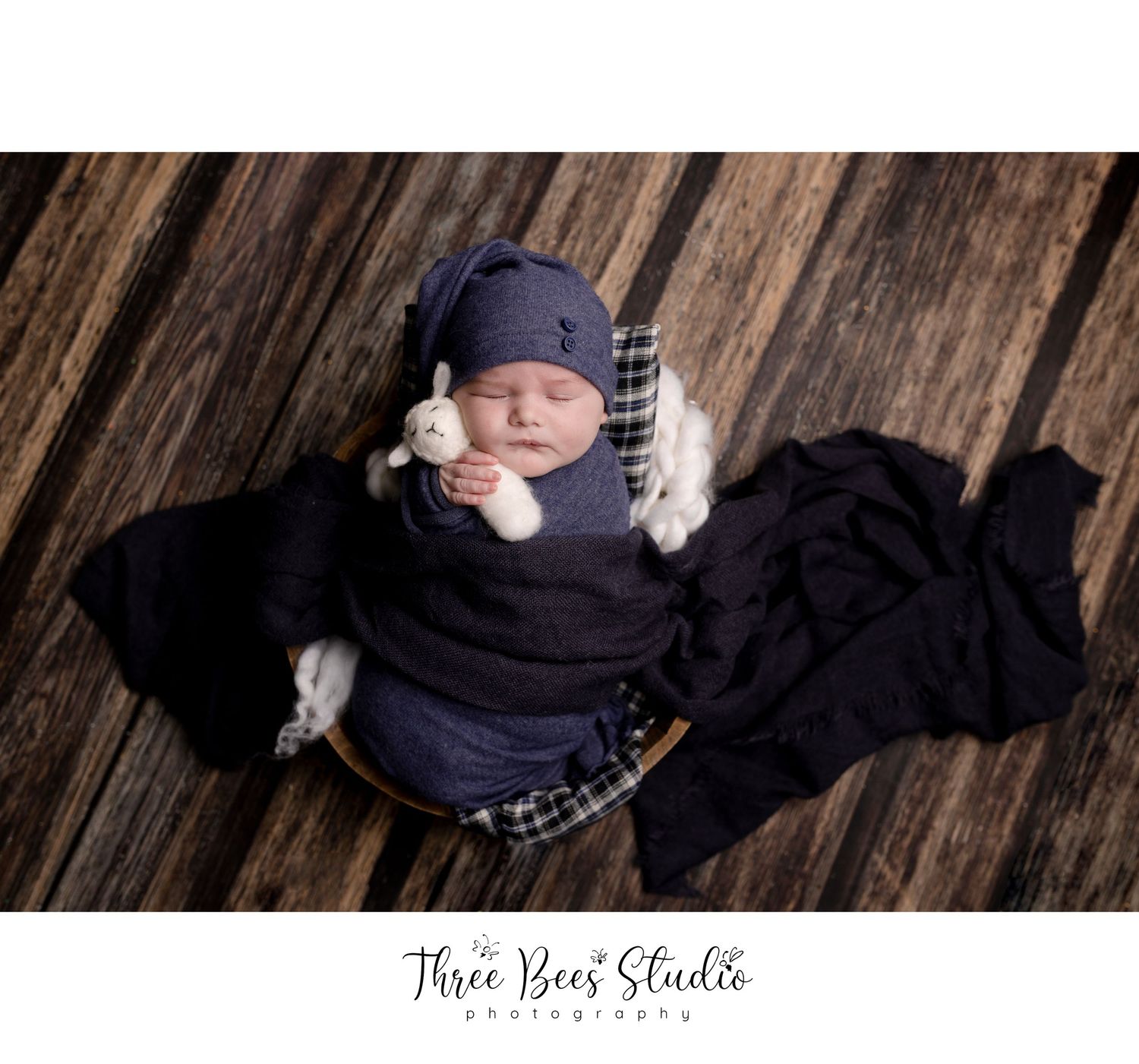 Sleeping newborn in navy outfit with plaid accents on wooden backdrop.