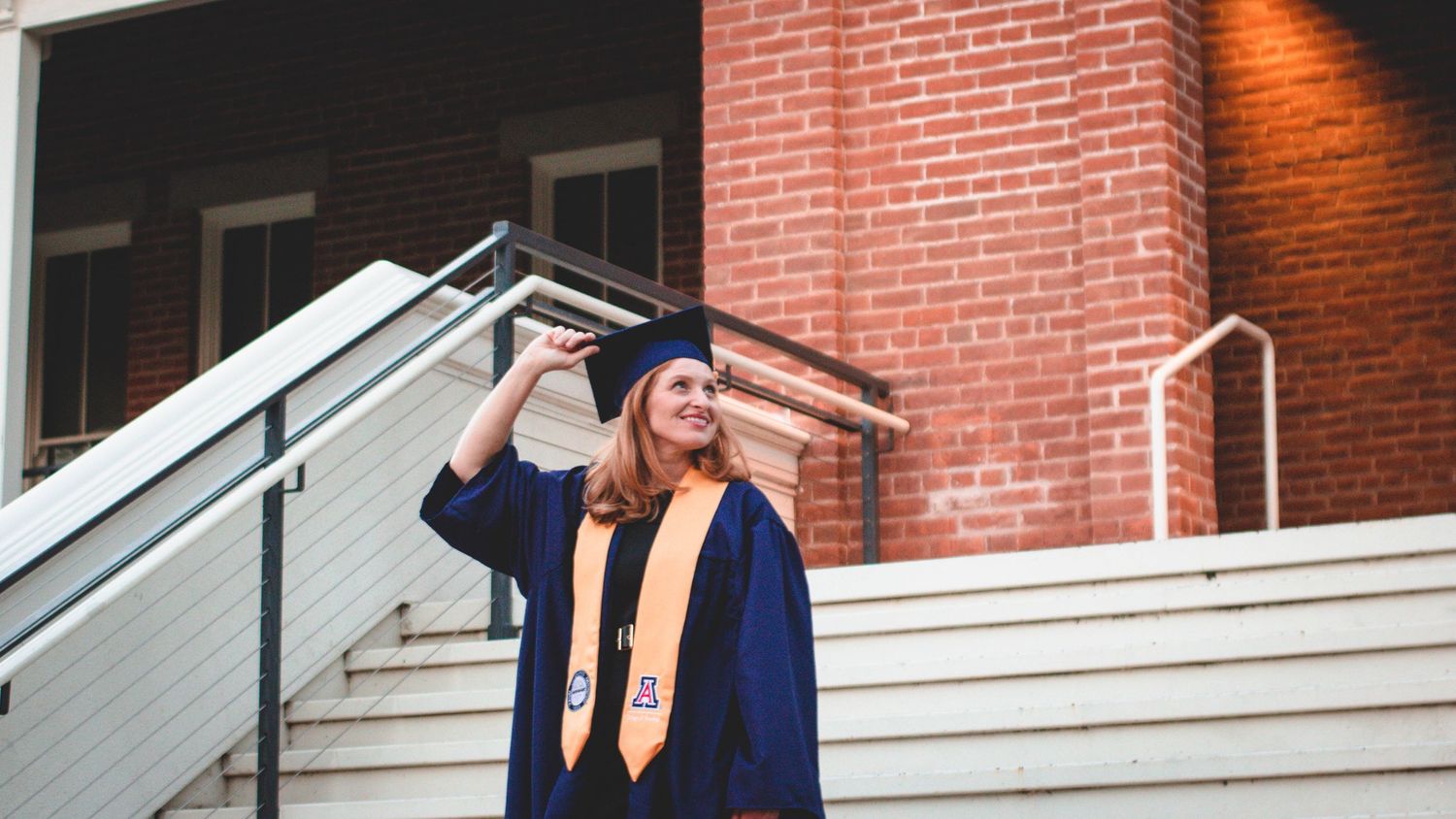 Graduate poses on brick steps and railings of campus building.