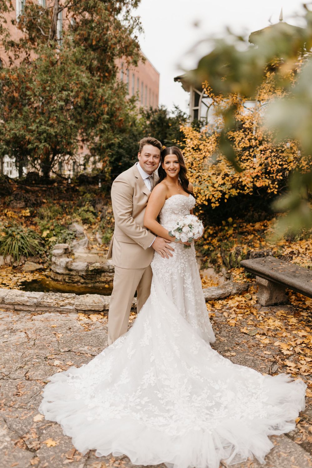 Bride and groom smile together in garden setting with yellow fall foliage framing the couple.