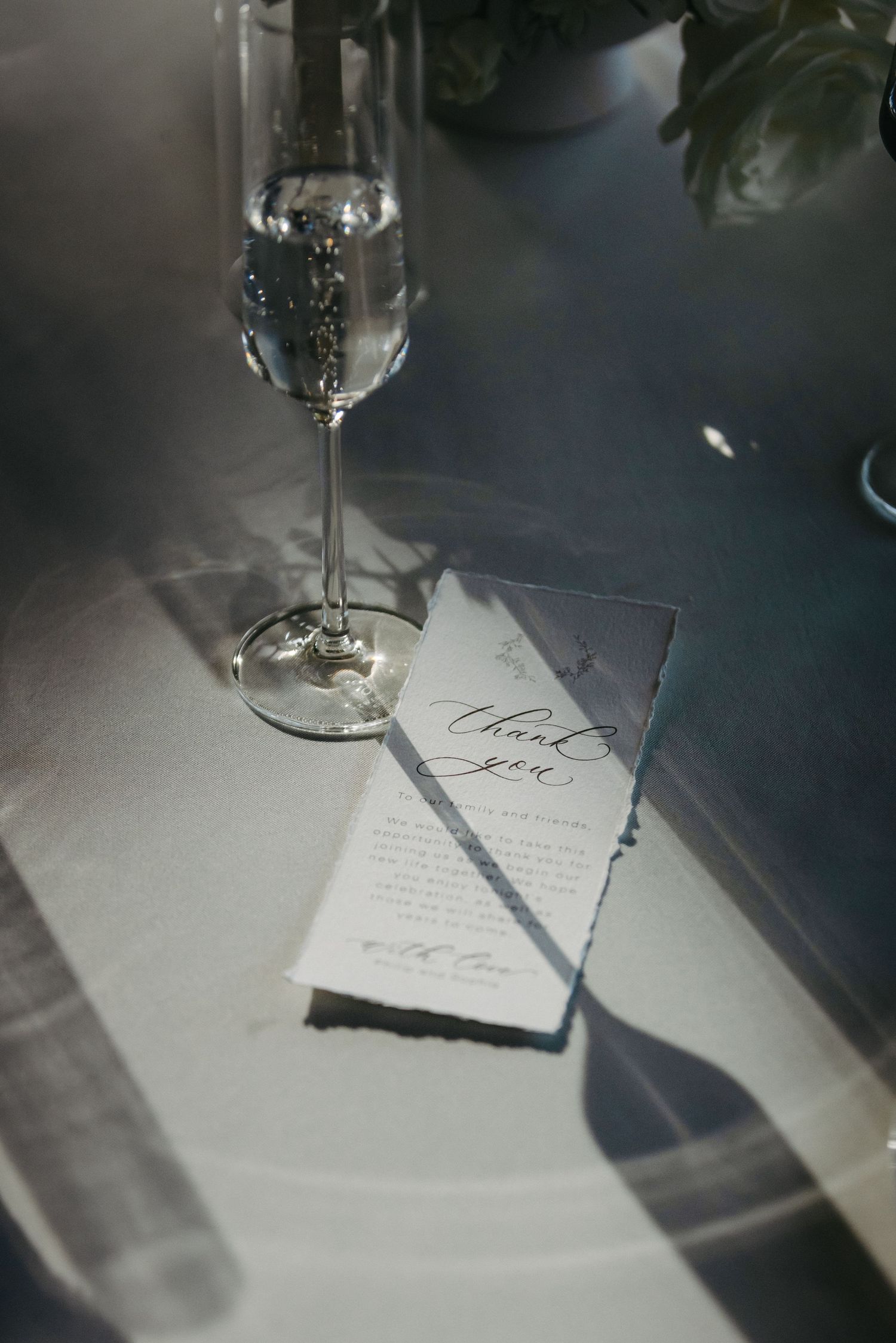 A champagne glass and handwritten menu card sitting on a white tablecloth in moody lighting.