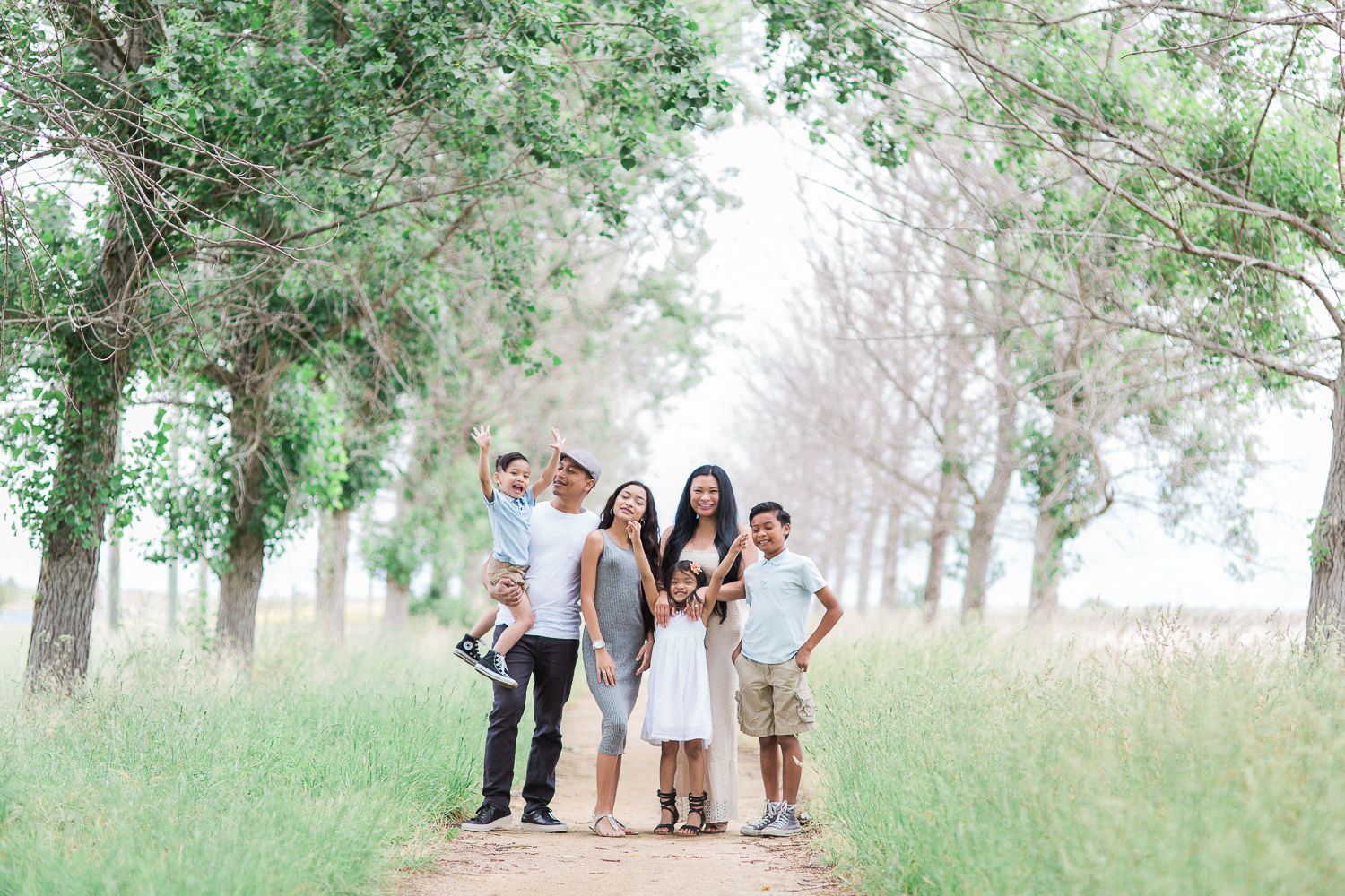 Family of four poses together on a tree-lined path in a serene outdoor setting.