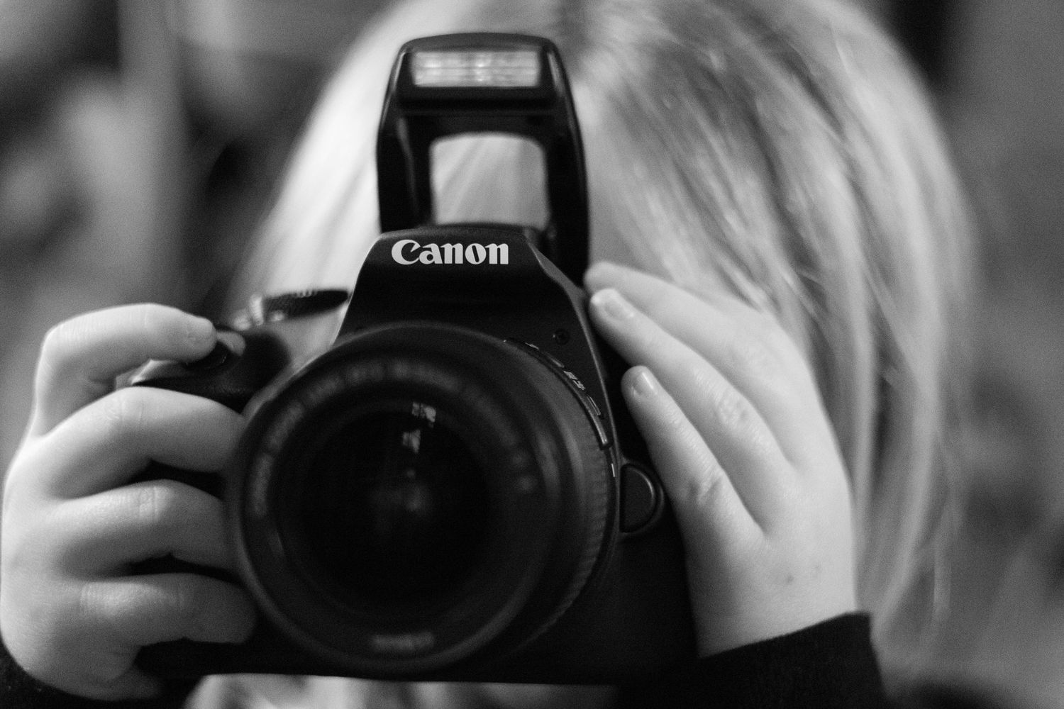 Black and white photo of hands holding a Canon DSLR camera.