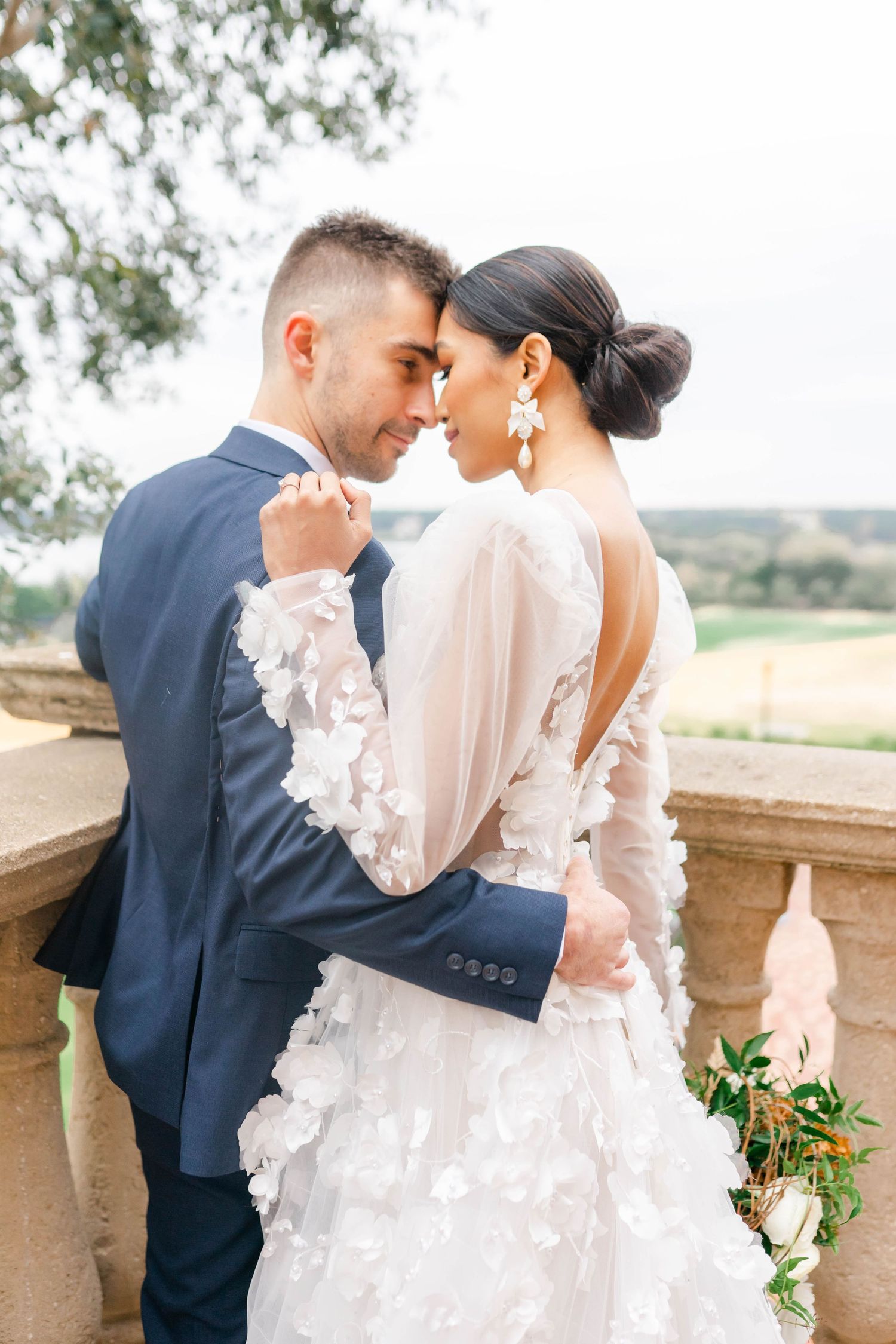 A bride and groom stand together on a brick patio, surrounded by lush greenery.