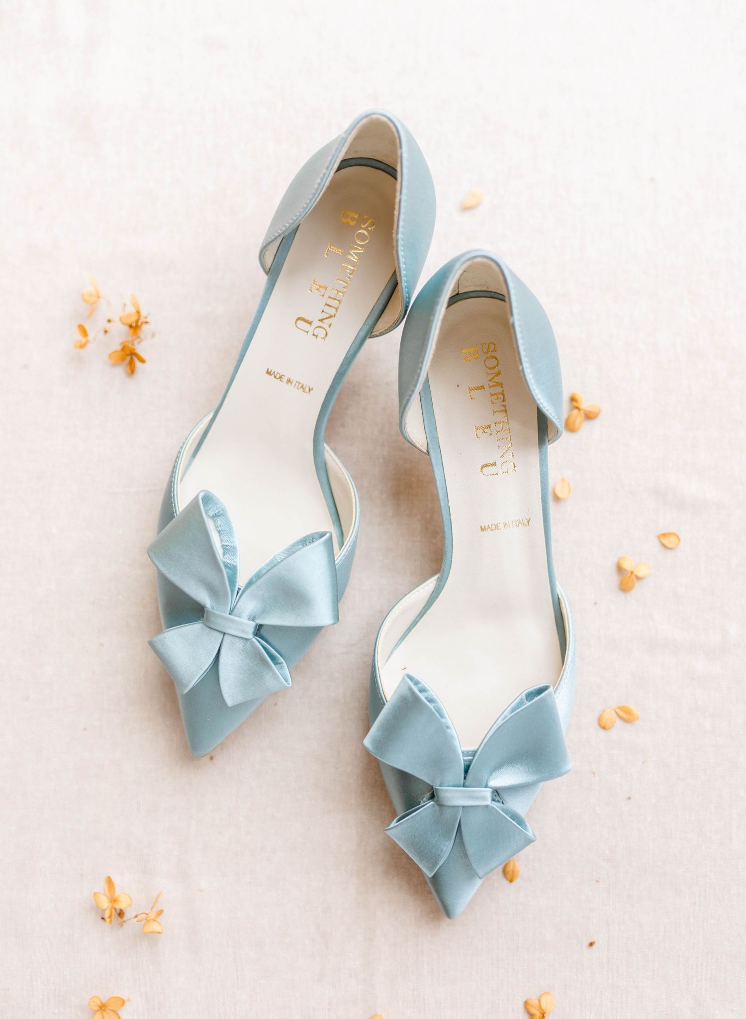 A pair of light blue high-heeled shoes with bows on the toes.