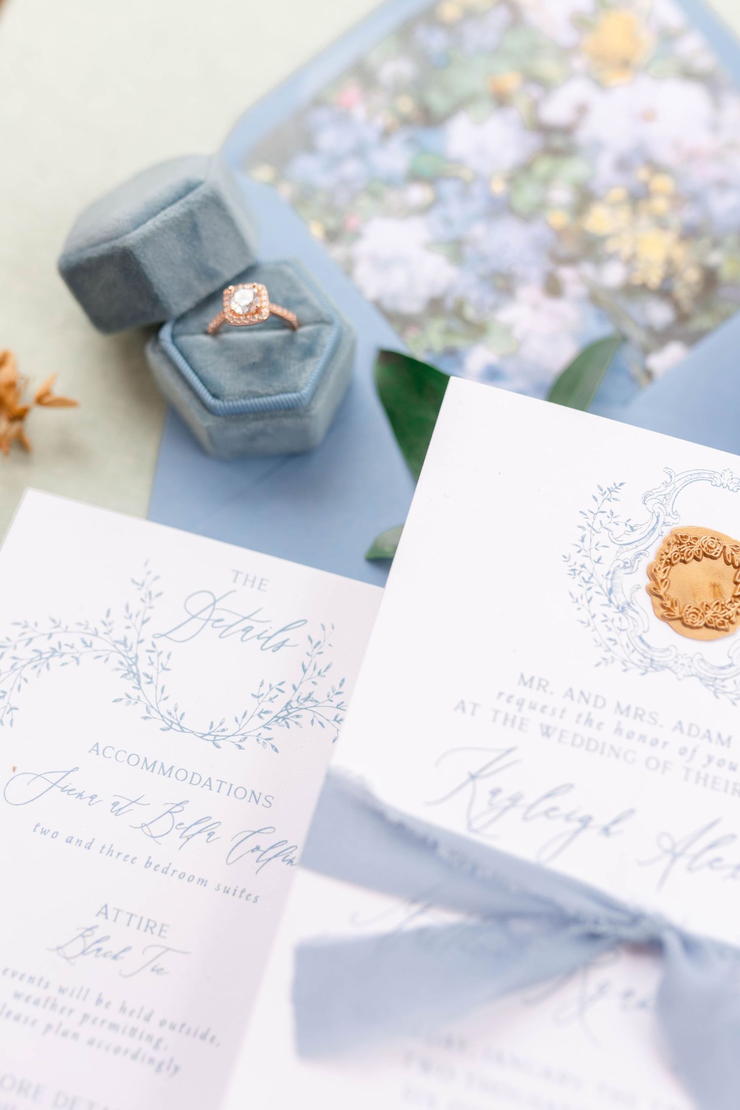 A close-up view of a wedding ring in a gray velvet box with a floral background.