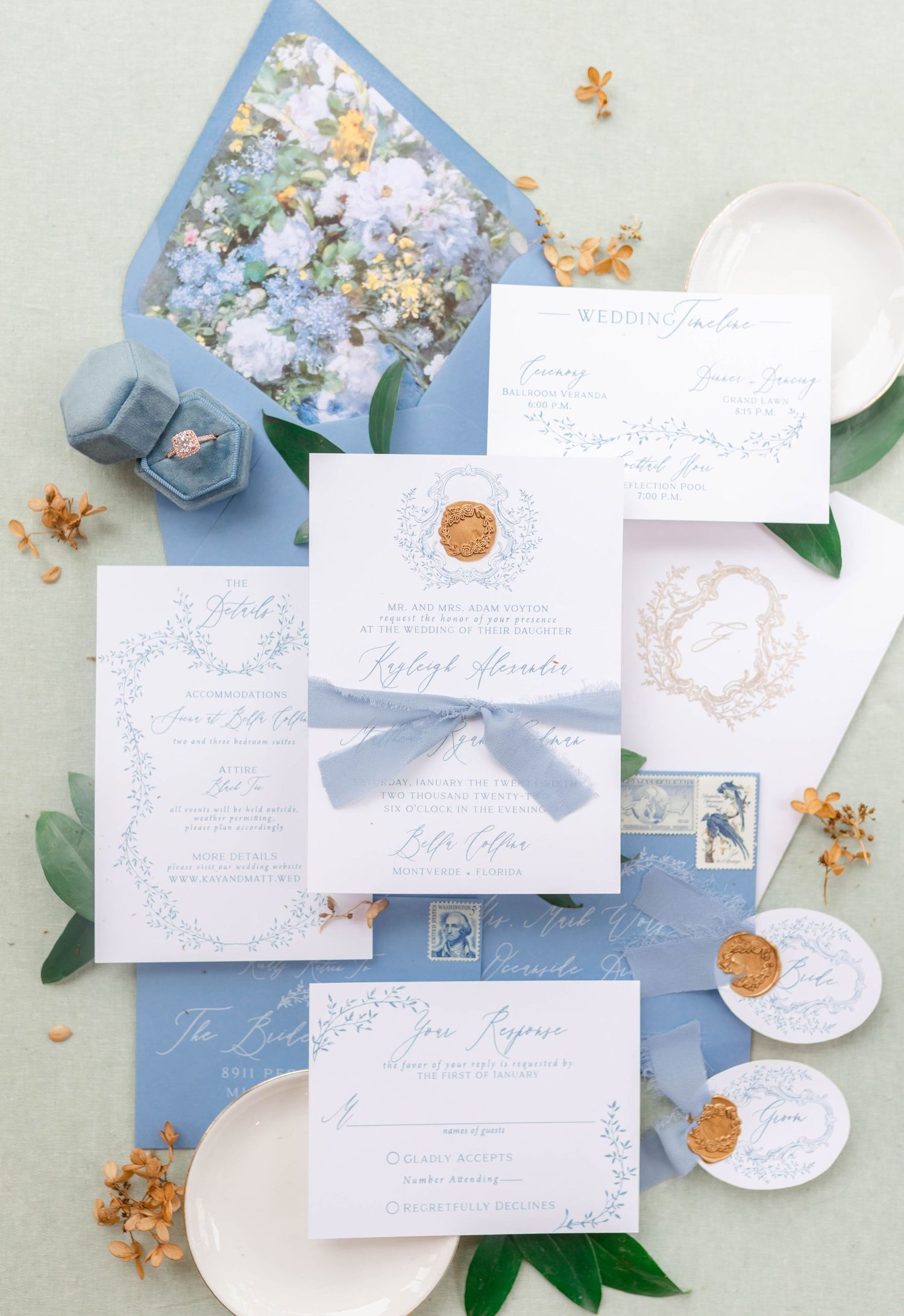 A wedding invitation suite with floral accents and a blue envelope.