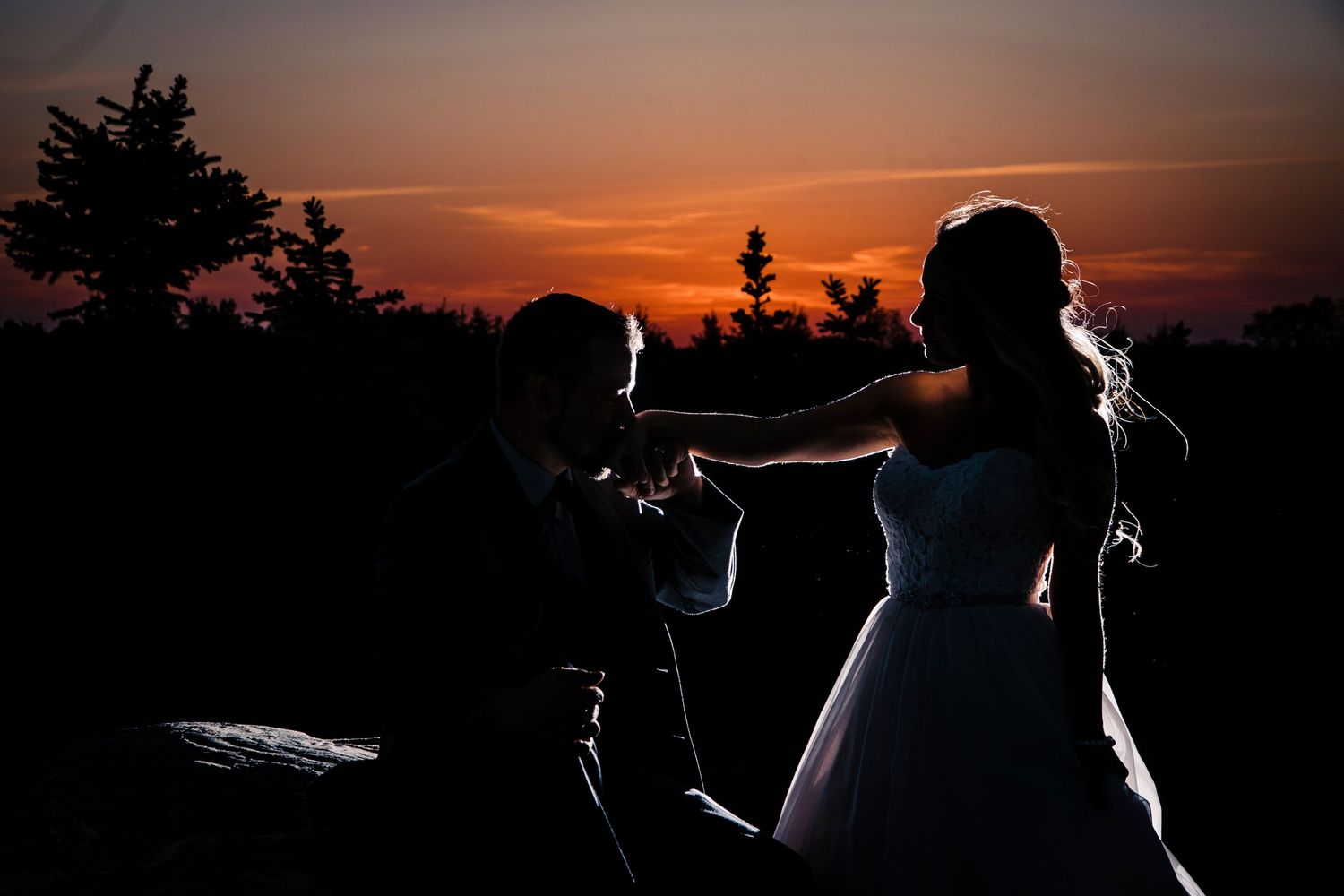 Silhouettes against vibrant orange and purple sunset sky during outdoor celebration.