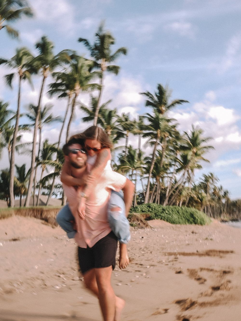 A couple playfully runs and embraces on a tropical beach with palm trees swaying in the background.