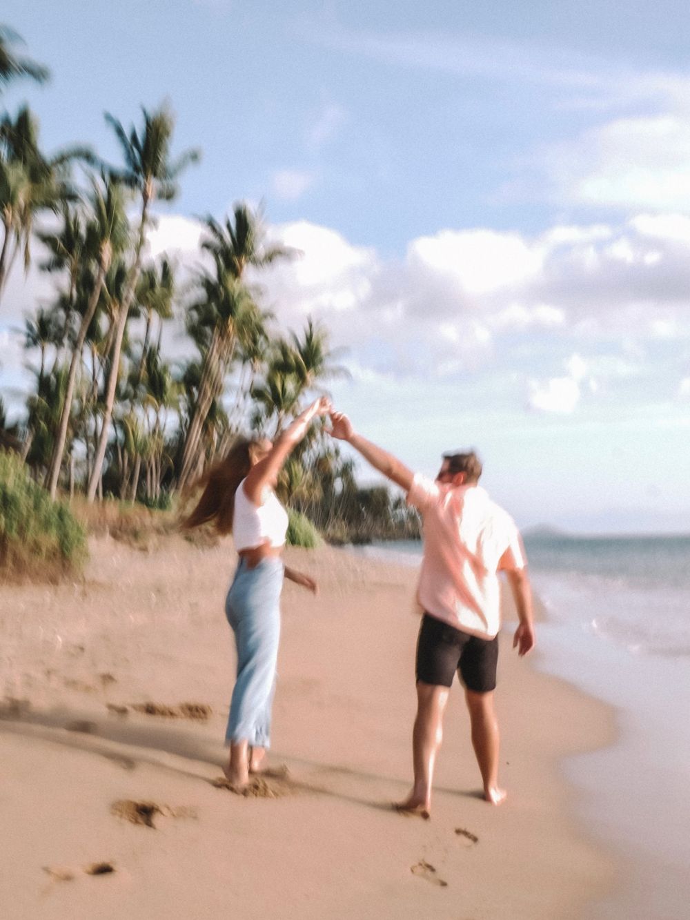 Two people dancing and having fun on a scenic beach with palm trees.