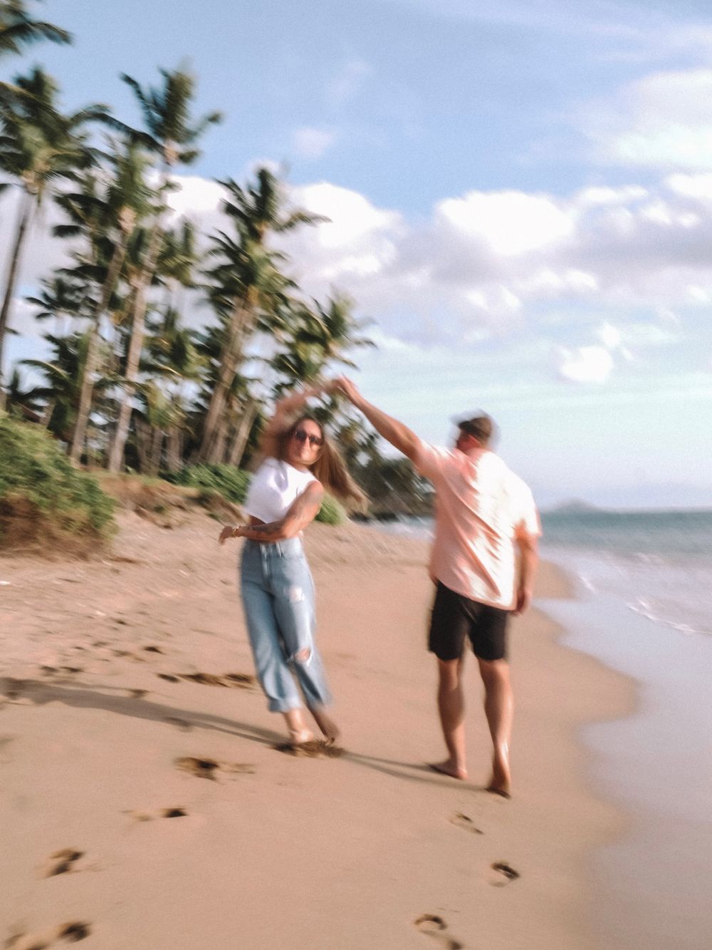 Couple enjoying a carefree moment on a tropical beach with swaying palm trees.