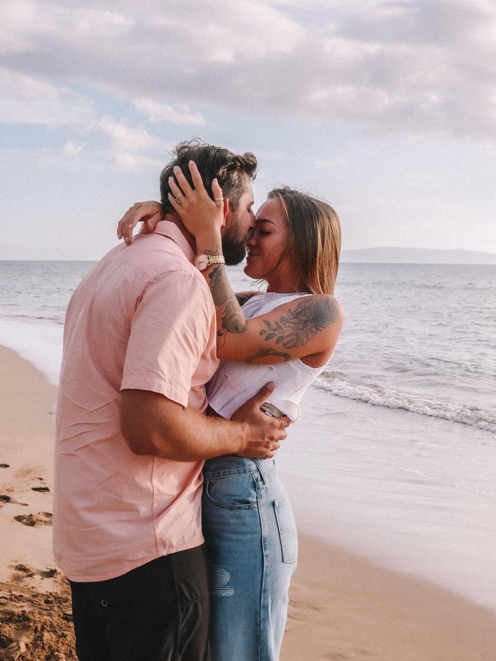 A tender beach photoshoot captures romantic moments between a couple by the ocean.