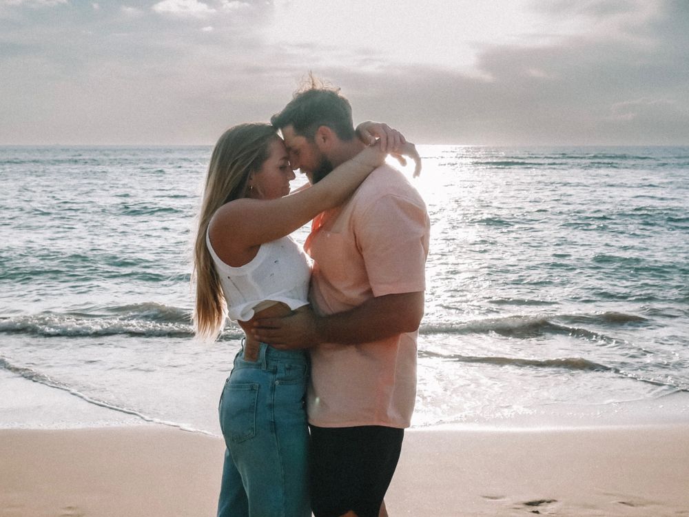 A romantic beach photoshoot features a couple embracing with waves crashing behind them.