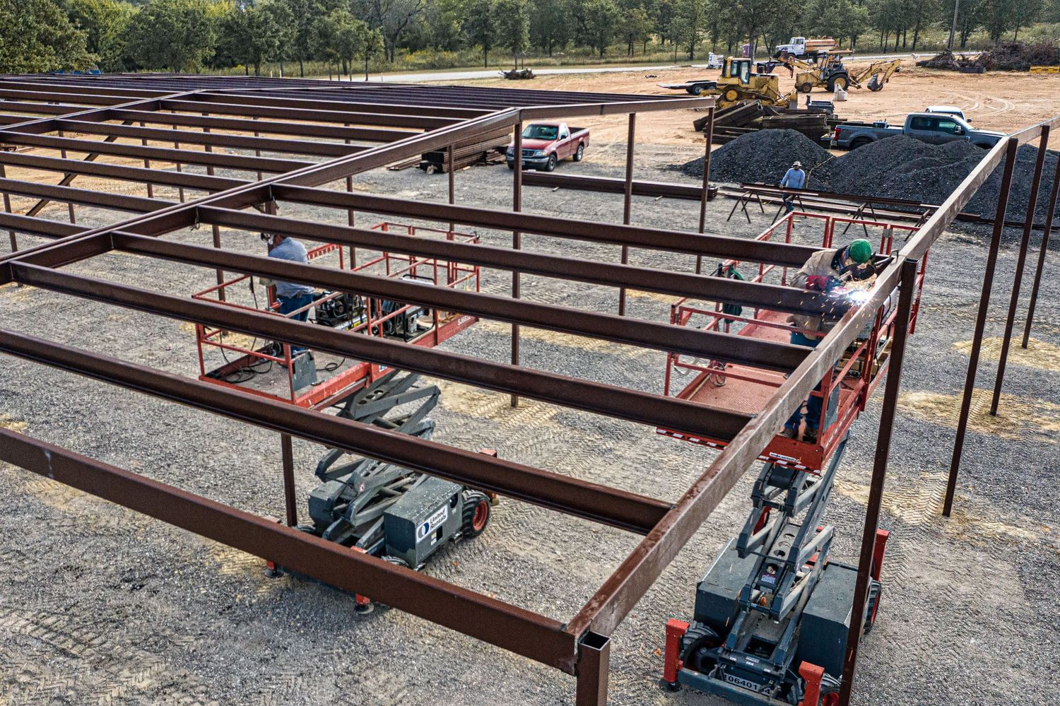The roof struts of a steel frame building are welded in place by workers in scissor lifts.