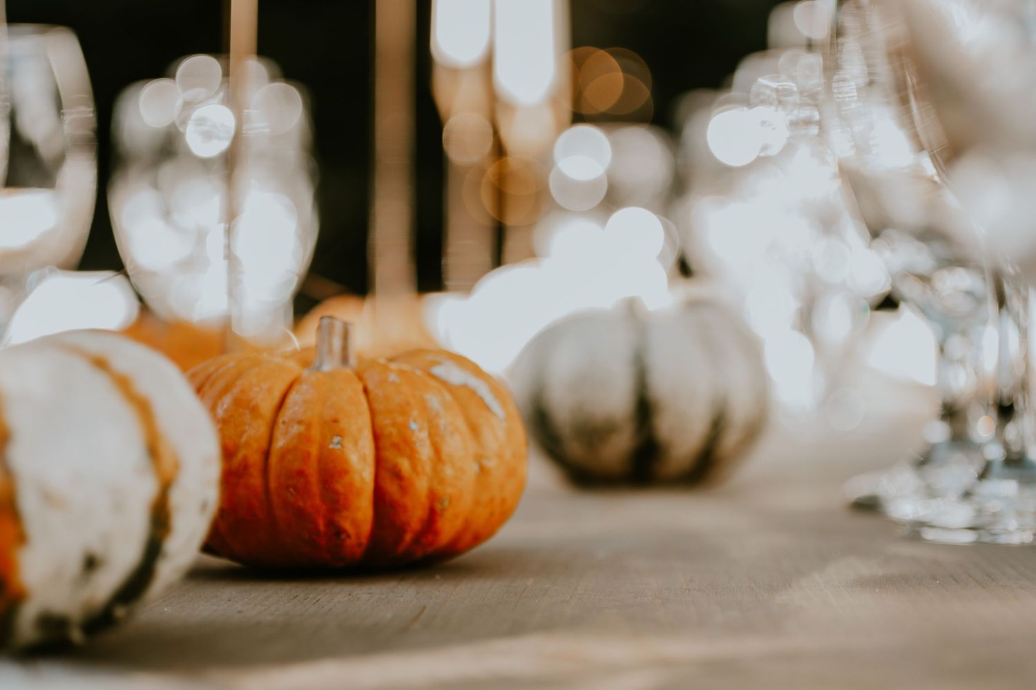 Small orange and white pumpkins decorate a table with glowing bokeh background.