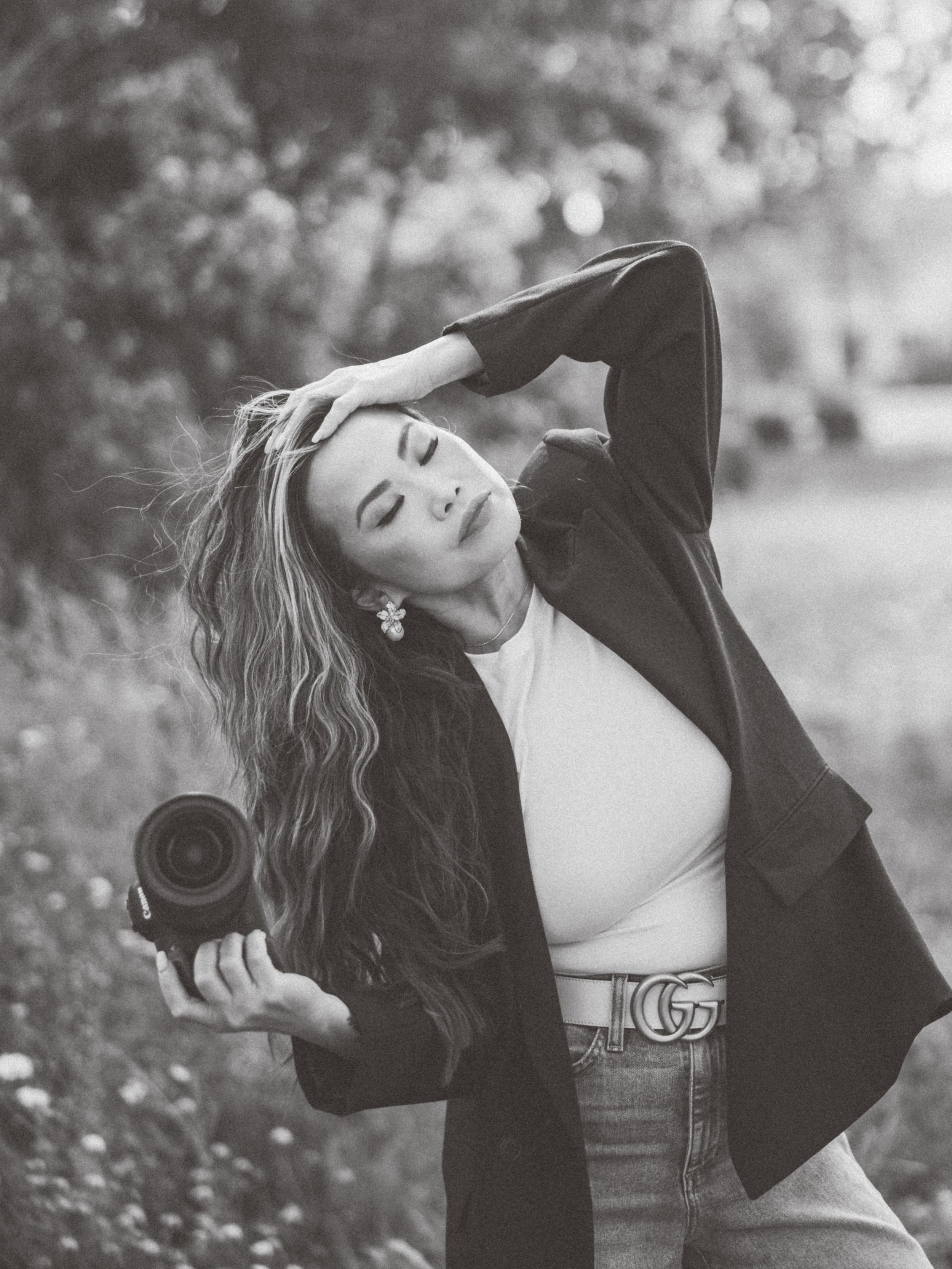 Artistic black and white photo of photographer posing with camera in casual attire.