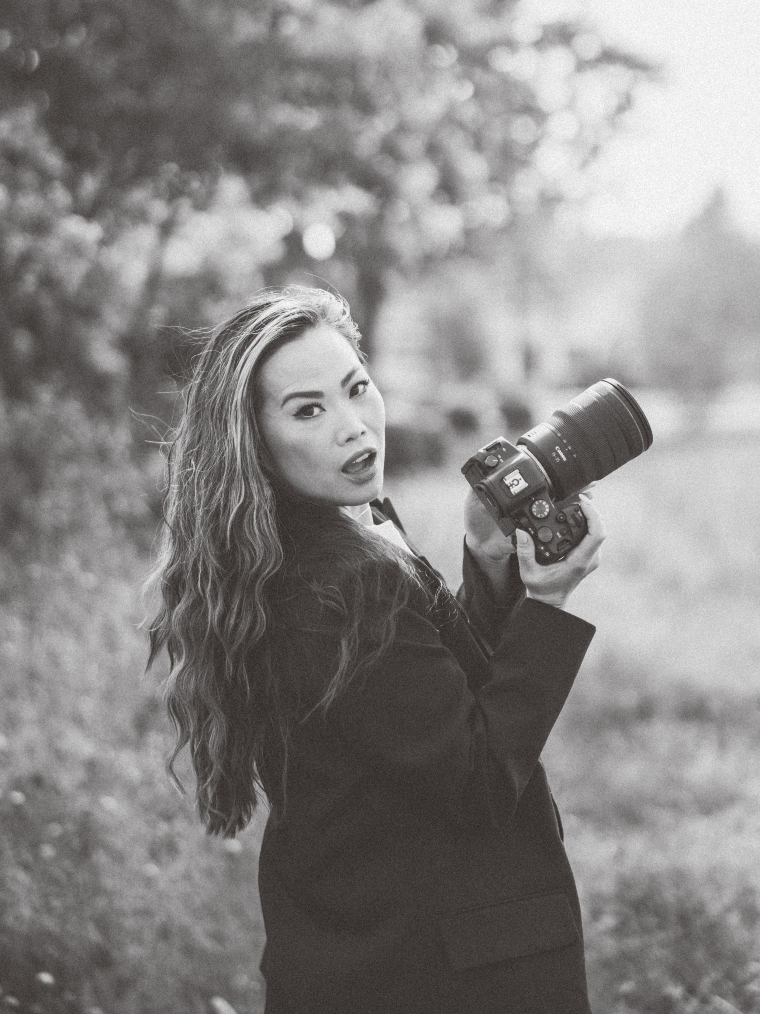 Dramatic black and white portrait of photographer with professional camera in outdoor setting.