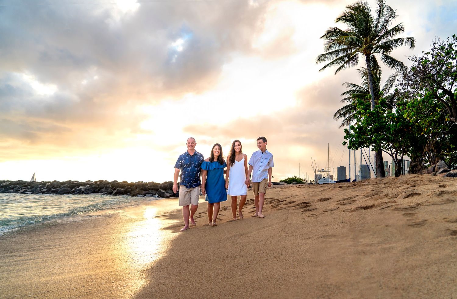 Family walks together along a tropical beach at sunset with palm trees in the background. Family Photography Hawaii