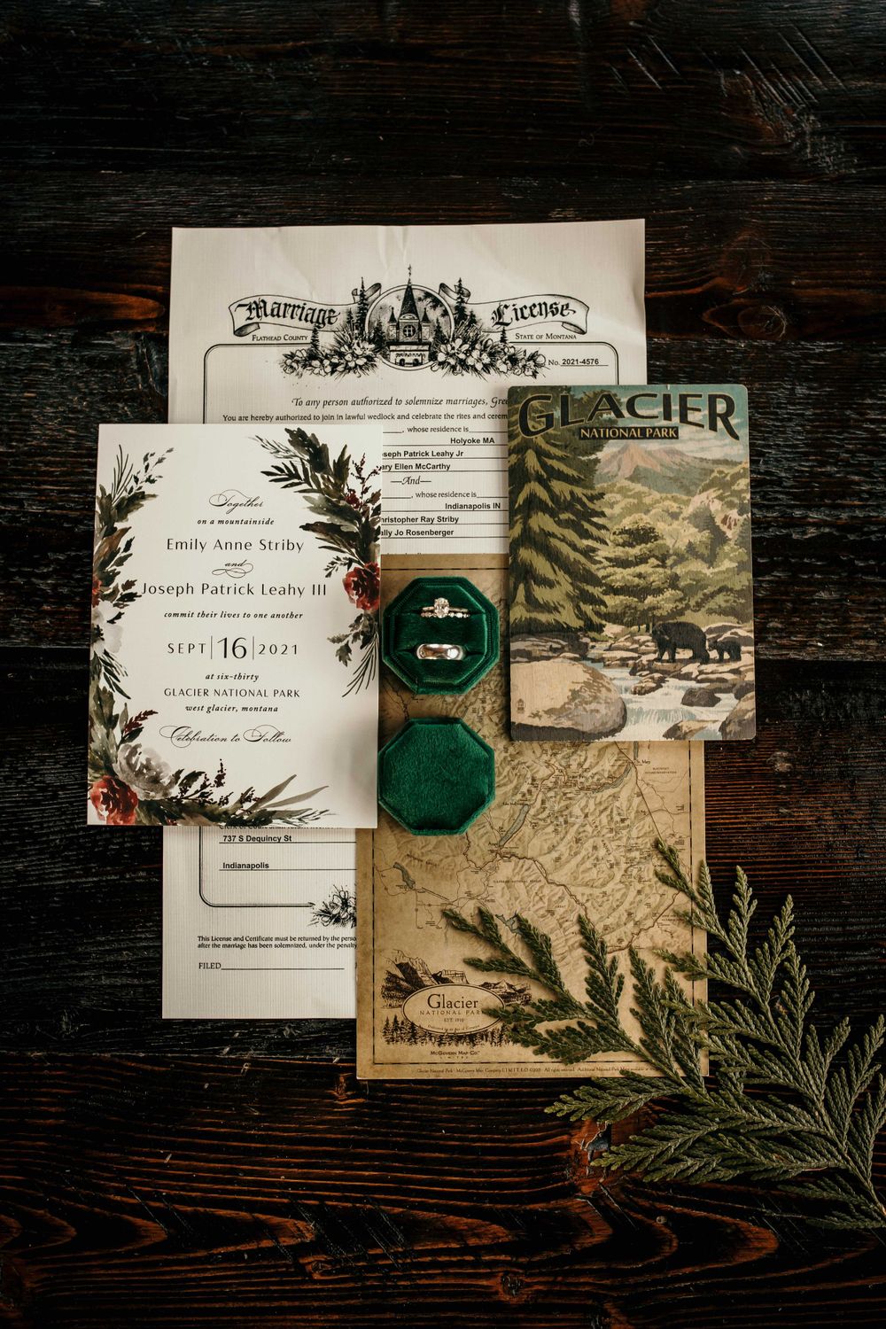 Wedding flat lay with marriage license, rings in green velvet box, and Glacier National Park map.