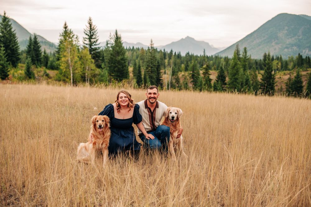 couple and their two dogs in a tall grass field with a mountain backdrop