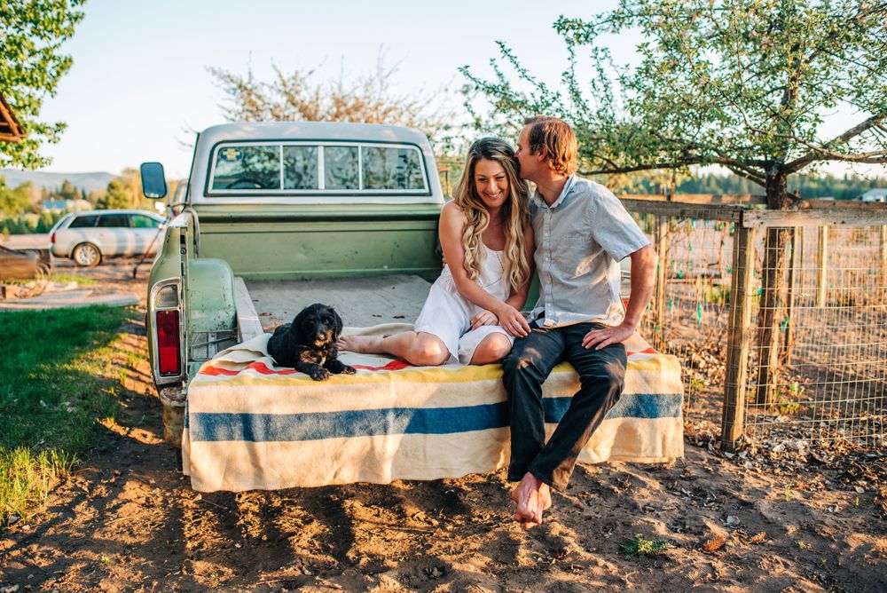 couple snuggling together in the back of a pick up truck, puppy sitting near them on the tailgate
