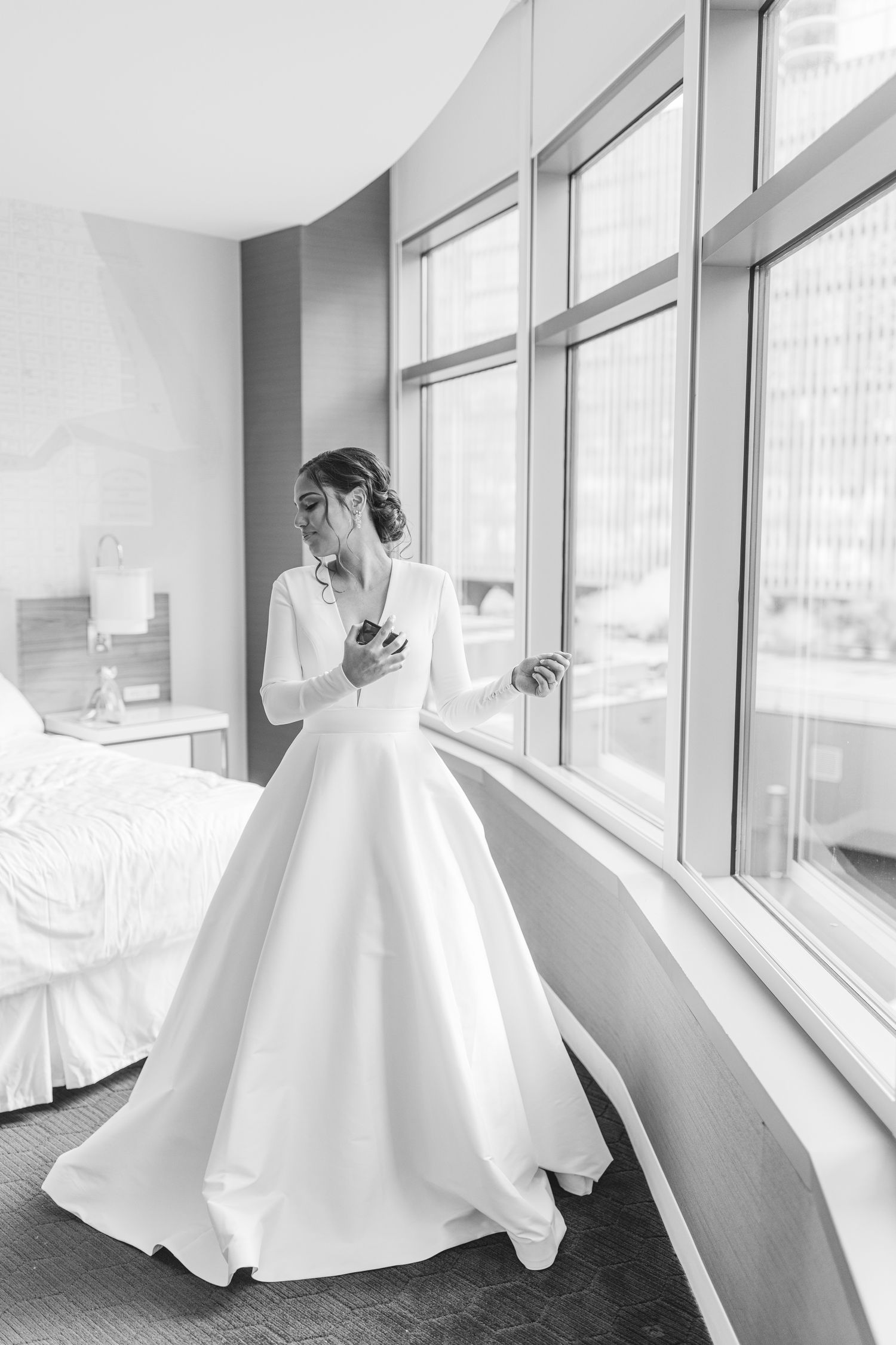 An elegant white wedding gown with long sleeves photographed in a sunlit hotel room.