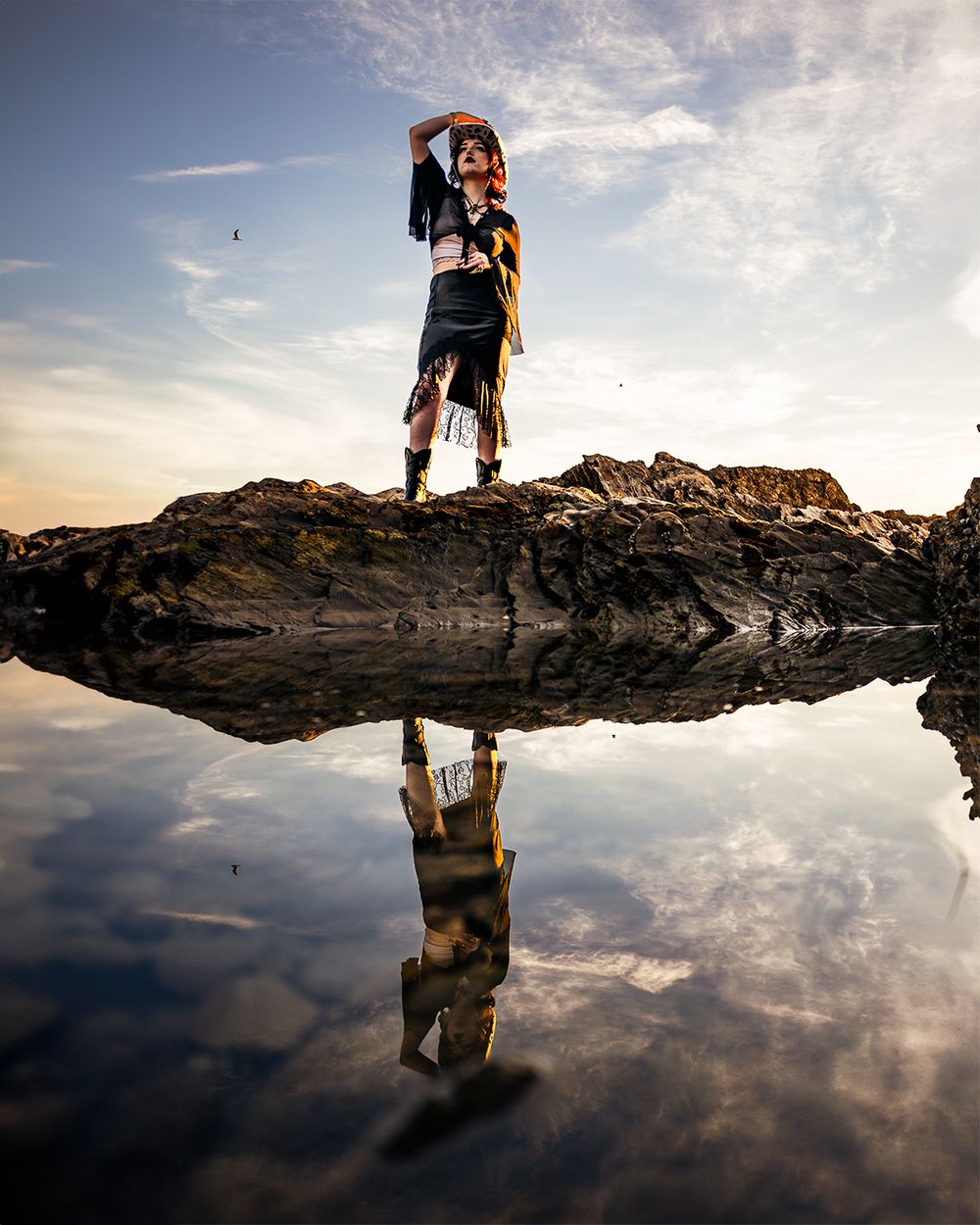 Fashion shoot of a female model by the Crystal Cove tide pools at sunset, featuring water reflections and a colorful sky.