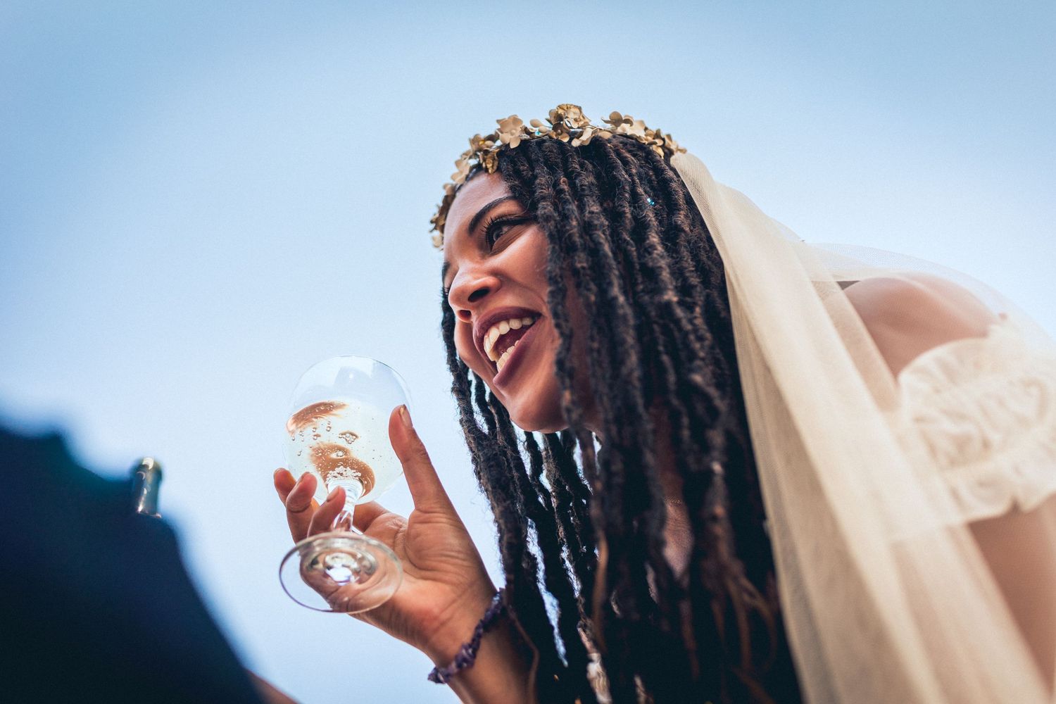 A joyful bride laughing while holding a champagne glass outdoors.