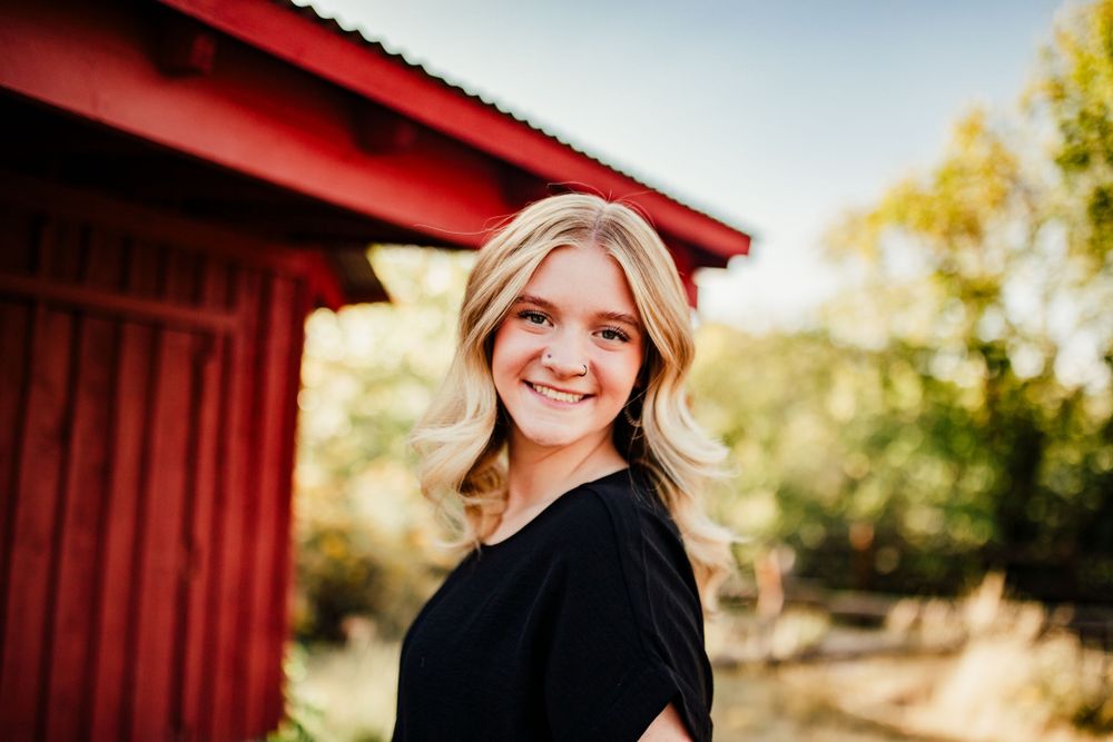 Portrait against a red barn wall in warm sunlight with soft natural expression.