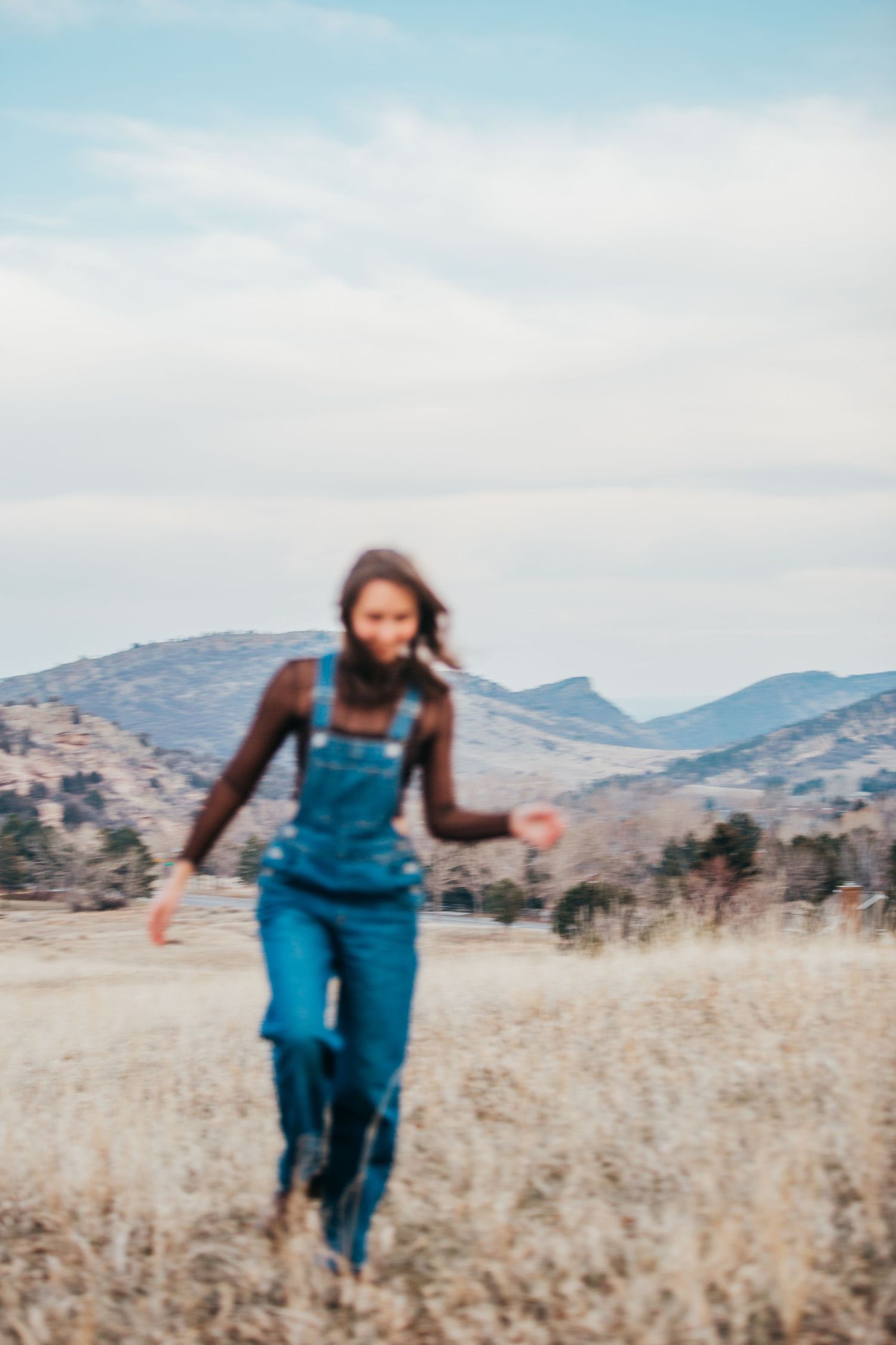 Motion shot of someone running through tall grass with mountains in background.