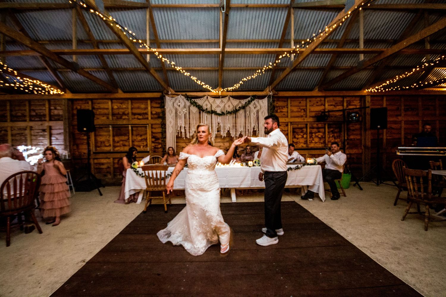 A couple performs a playful dance move on a wooden floor in a barn-style wedding venue.