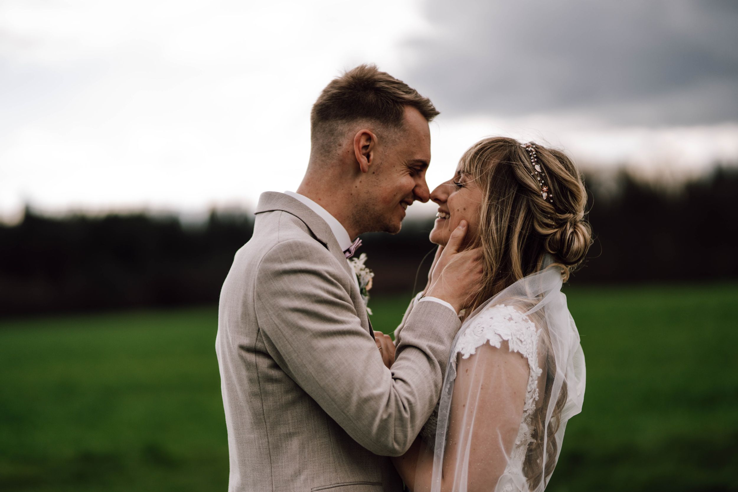 Newlyweds sharing intimate moment in outdoor field setting.