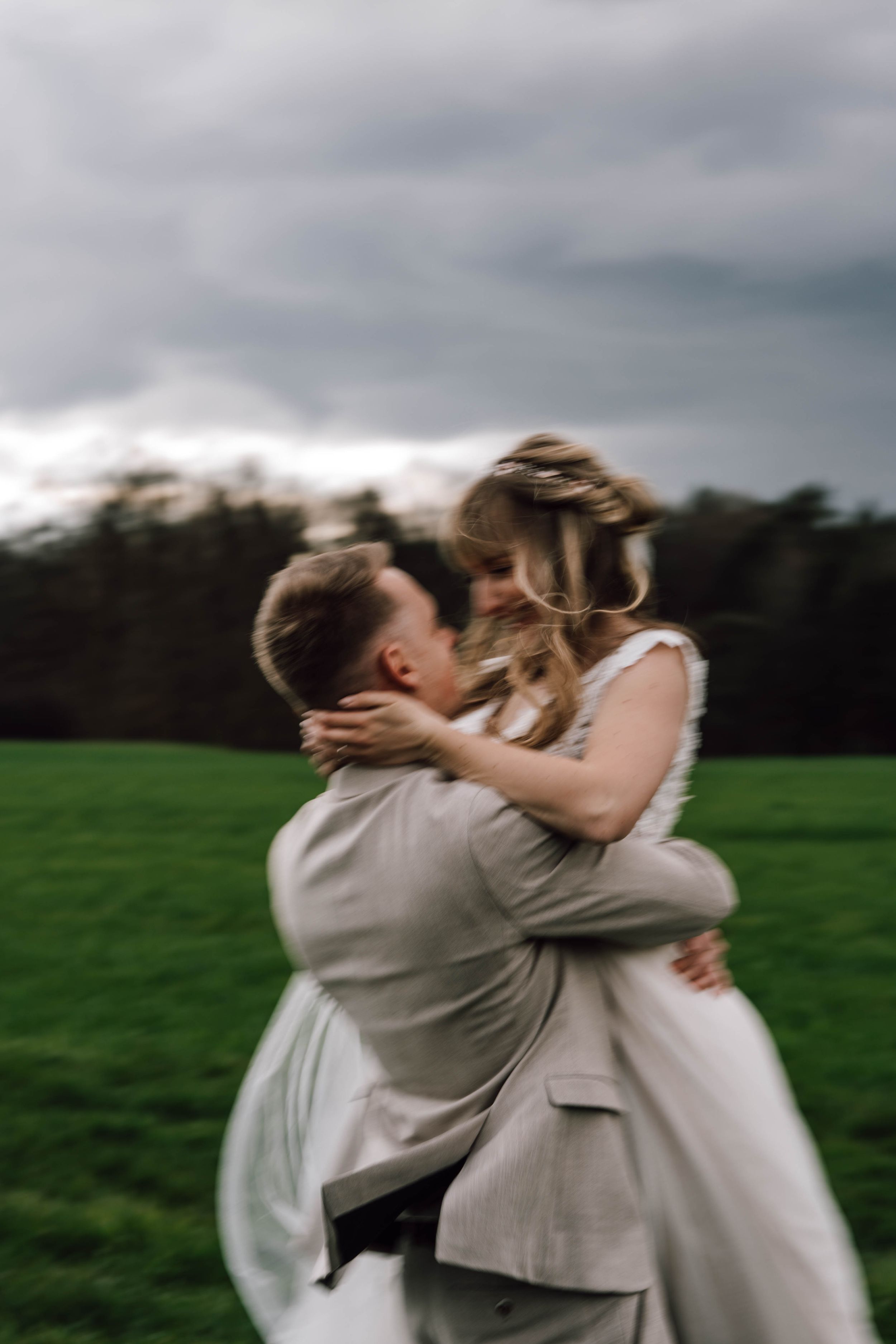 Wedding couple embracing and laughing together in green field.